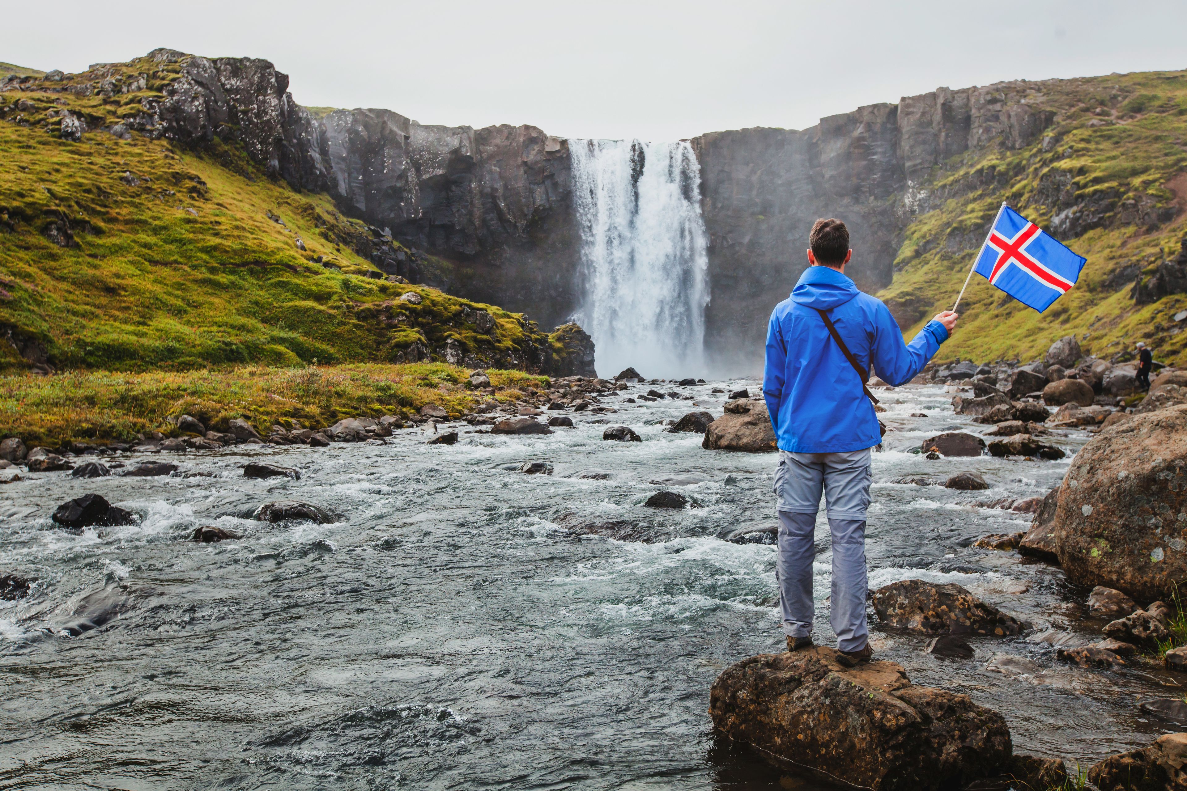 Chico sosteniendo la bandera de Islandia en frente de una cascada