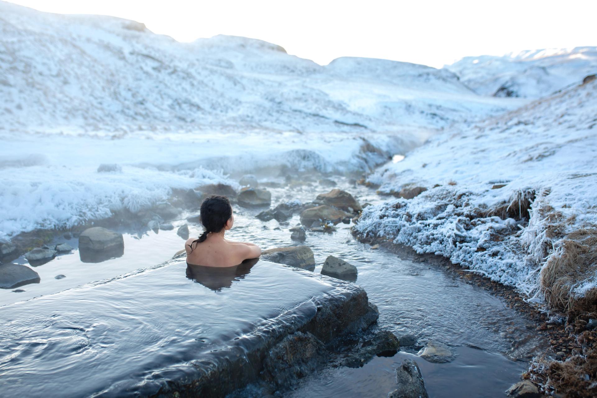 Woman in a hot spring in Iceland watching the sun rises during a chilly weather