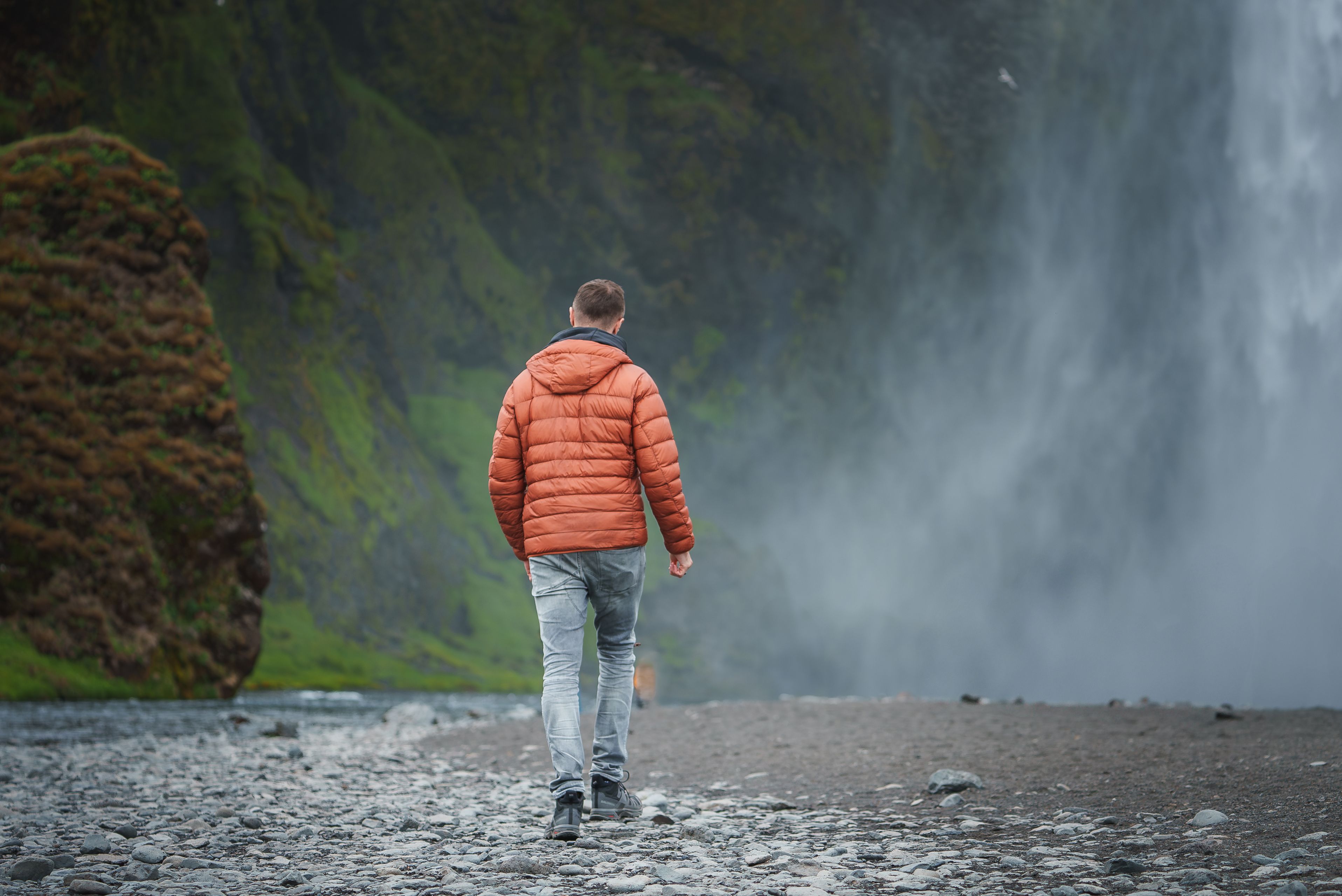 Man with jeans and a waterproof jacket walking towards Skógafoss Waterfall in Iceland