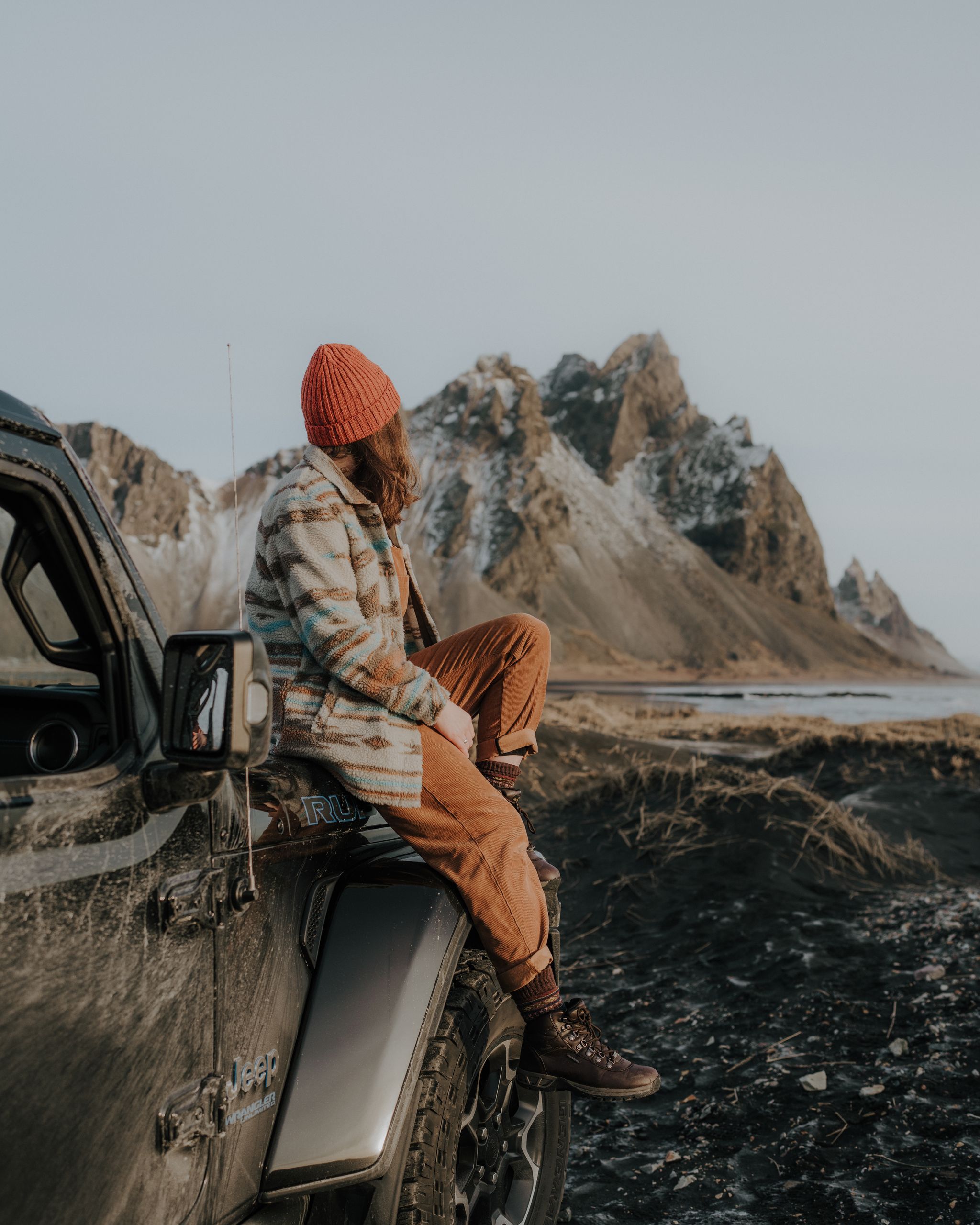 Woman sitting on her iceland rental car watching the mountain from a far away