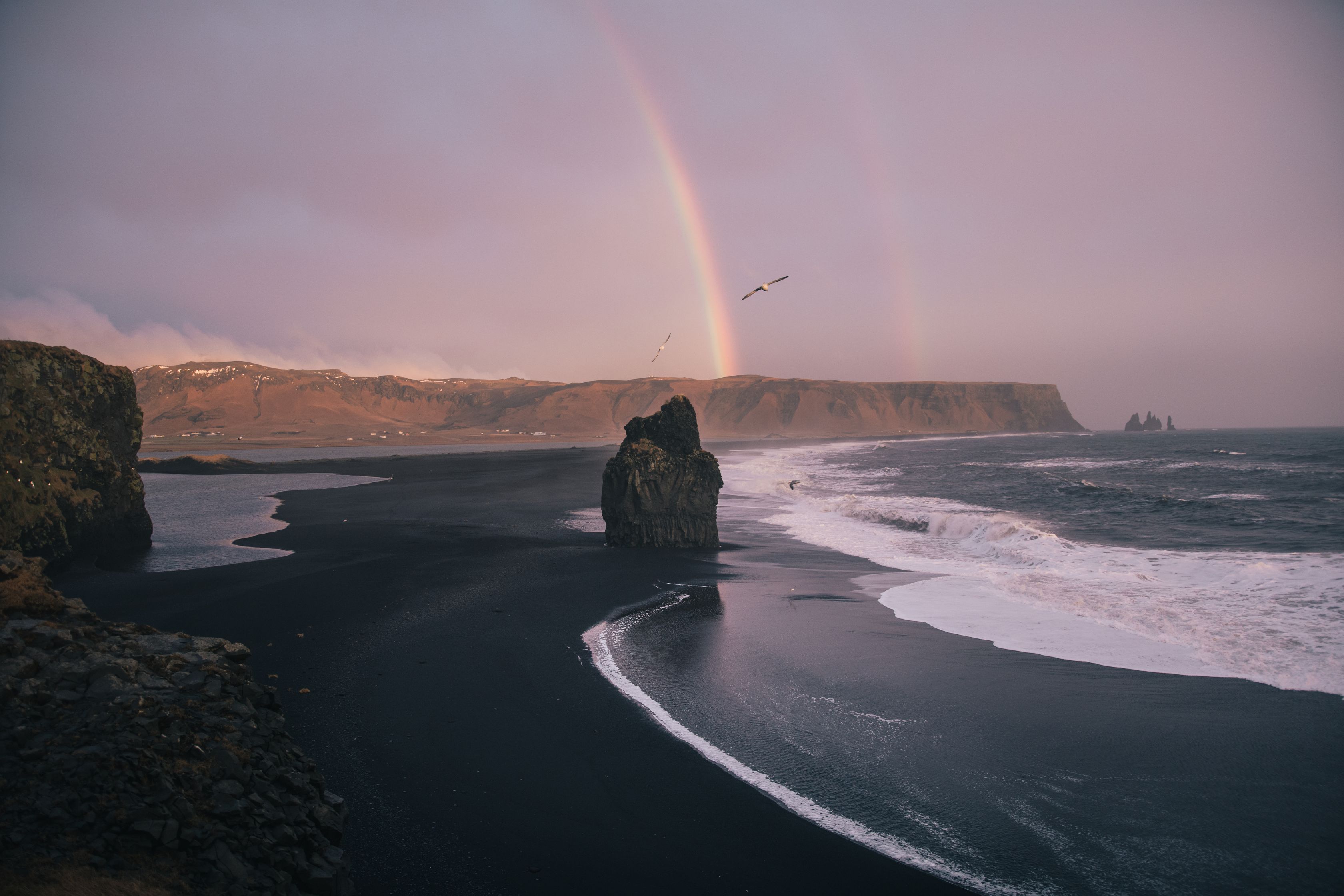 Long black sand beach with a massive rainbow in Iceland