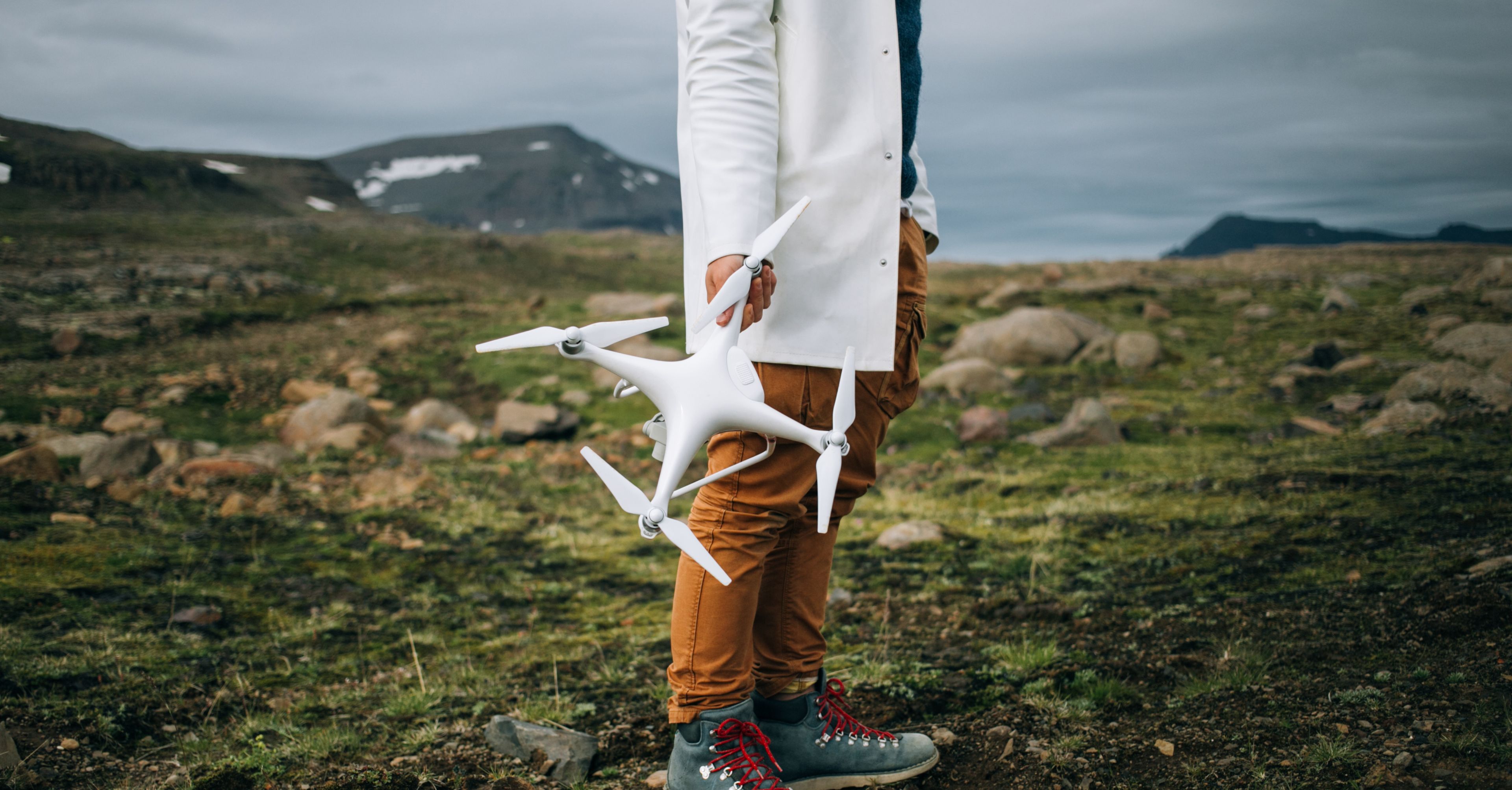 A man stands on a rocky surface in Iceland during an epic journey, holding a large professional drone.