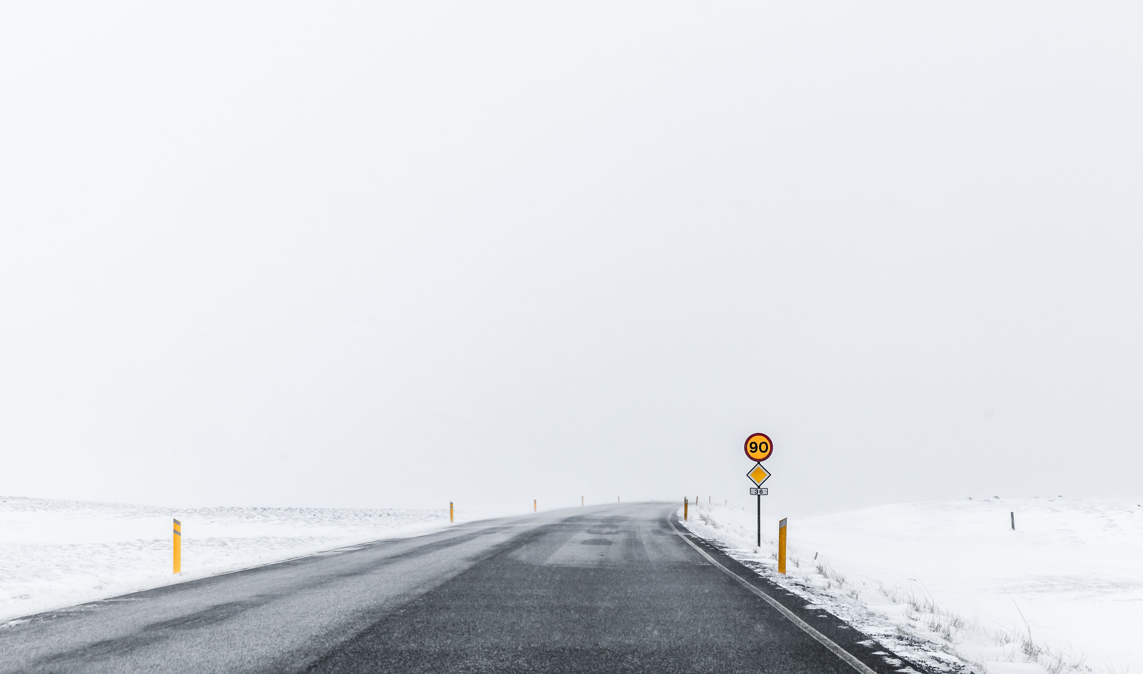 A paved snowy road in Iceland, marked by a speeding sign
