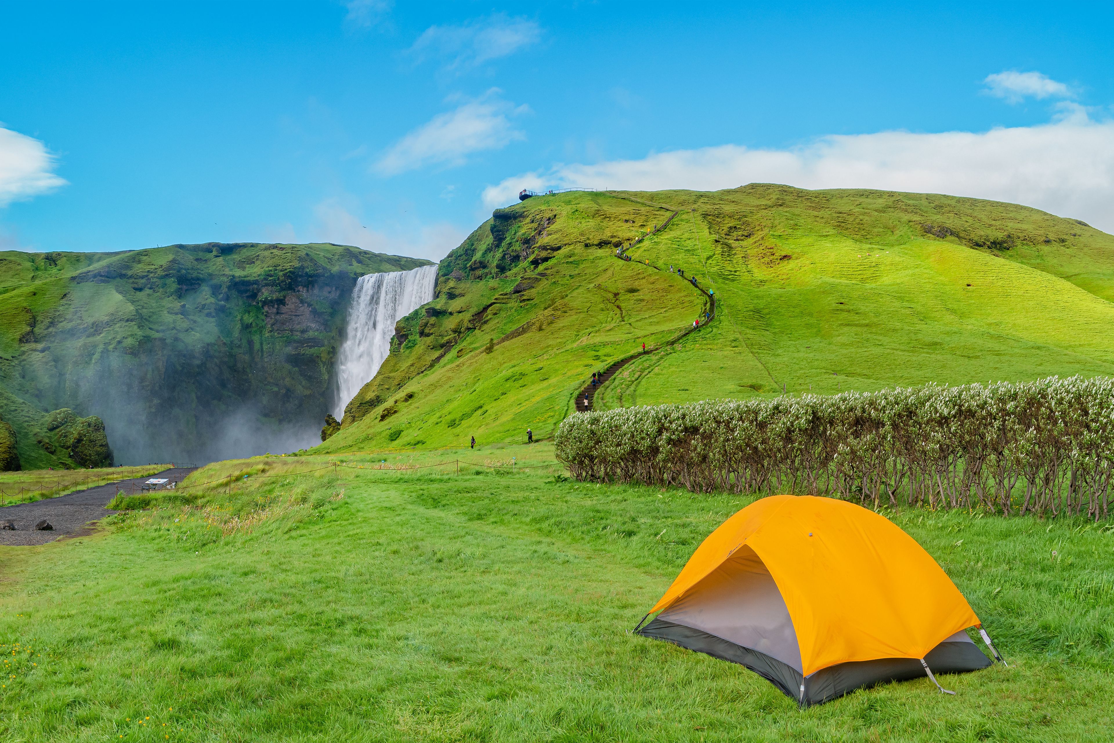 Panoramic view over camping site with orange tent, and tourists in front of famous Skogafoss waterfall, while hiking in Iceland, summer, scenic view.