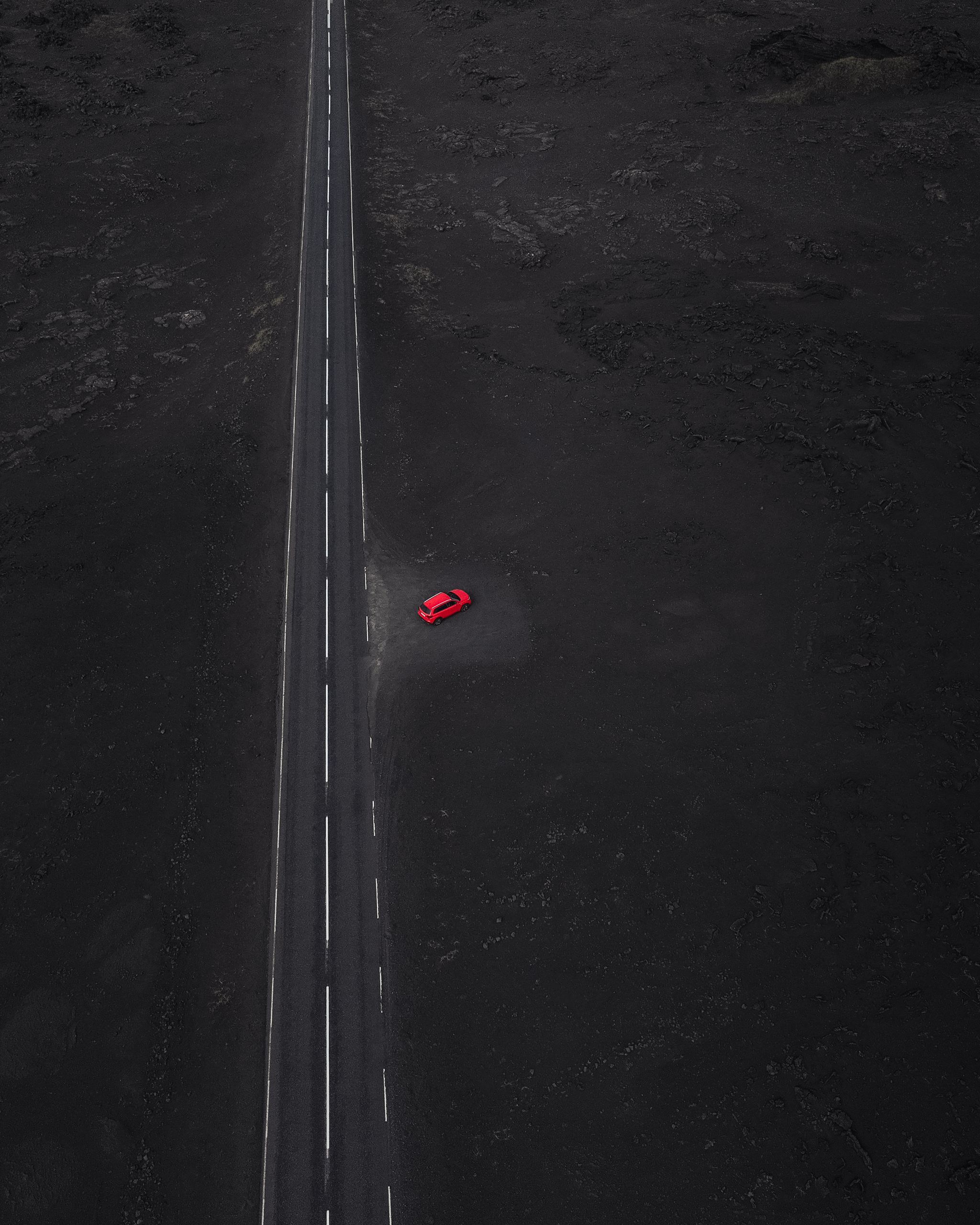 Ein roter Vitara-Mietwagen, geparkt an einer Straße mit Lavafelsen drum herum