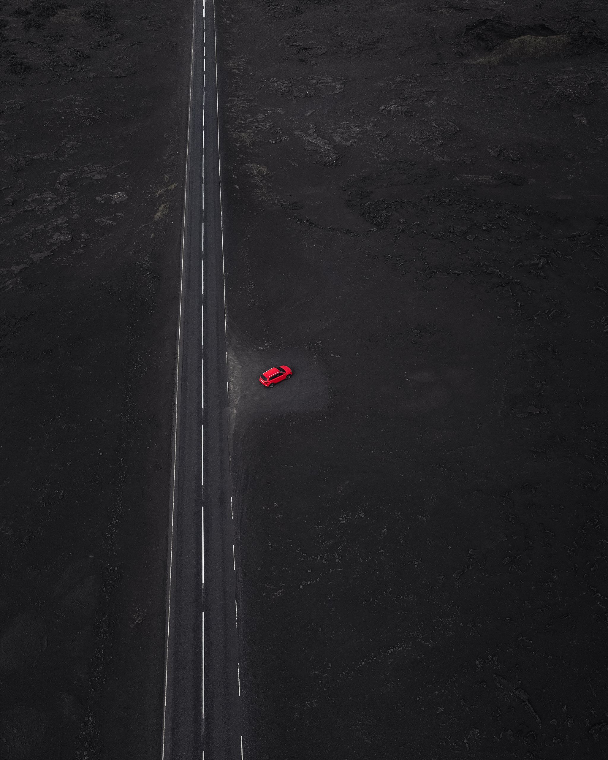一辆红色的维塔拉租车停在一条靠近道路的地方，周围是熔岩石。