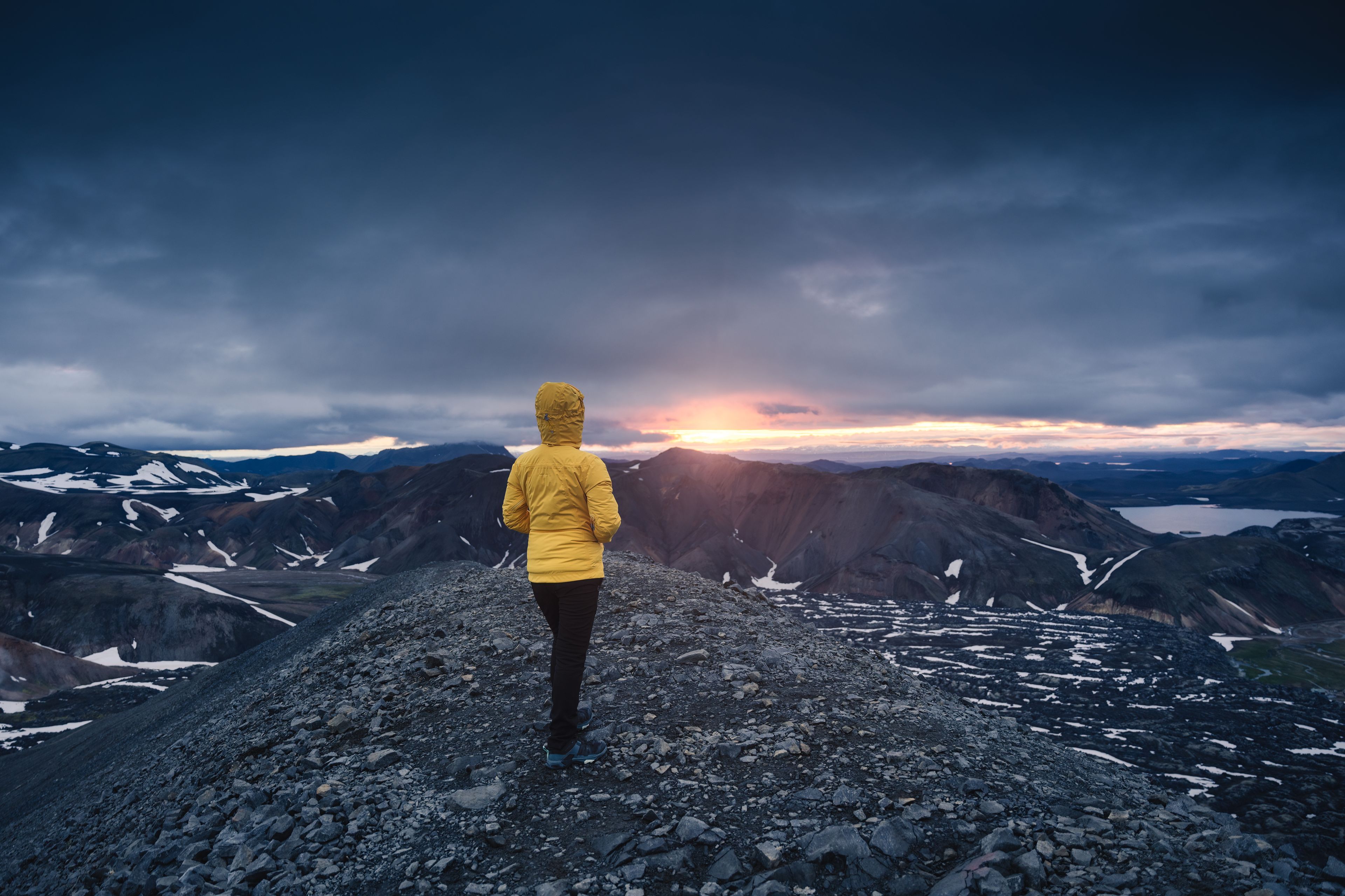 Mujer excursionista con chaqueta amarilla en una montaña volcánica durante el Sol de Medianoche en el sendero Bláhnjúkur en las tierras altas de Islandia