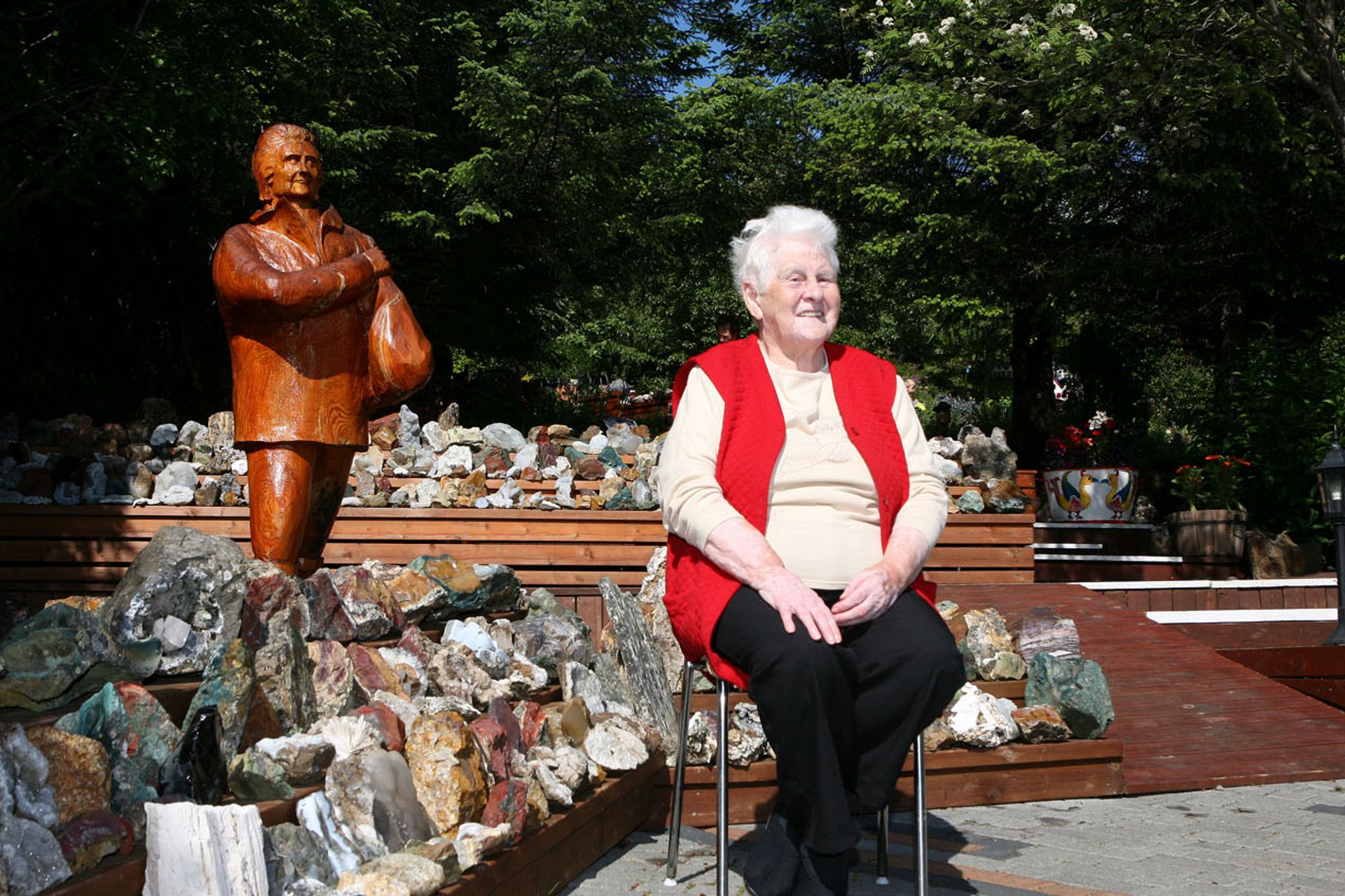 Picture of Petra during summer, sitting on a chair, proud of her garden and her stone collection 