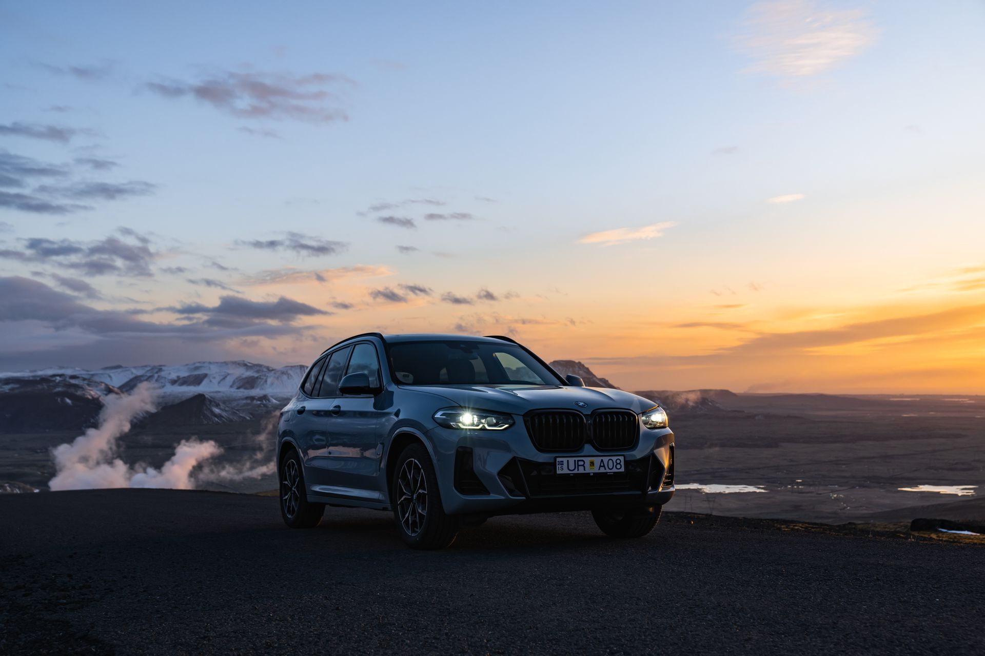 Coche BMW X3 gris oscuro aparcado en la cima de una montaña bajo una puesta de sol islandesa