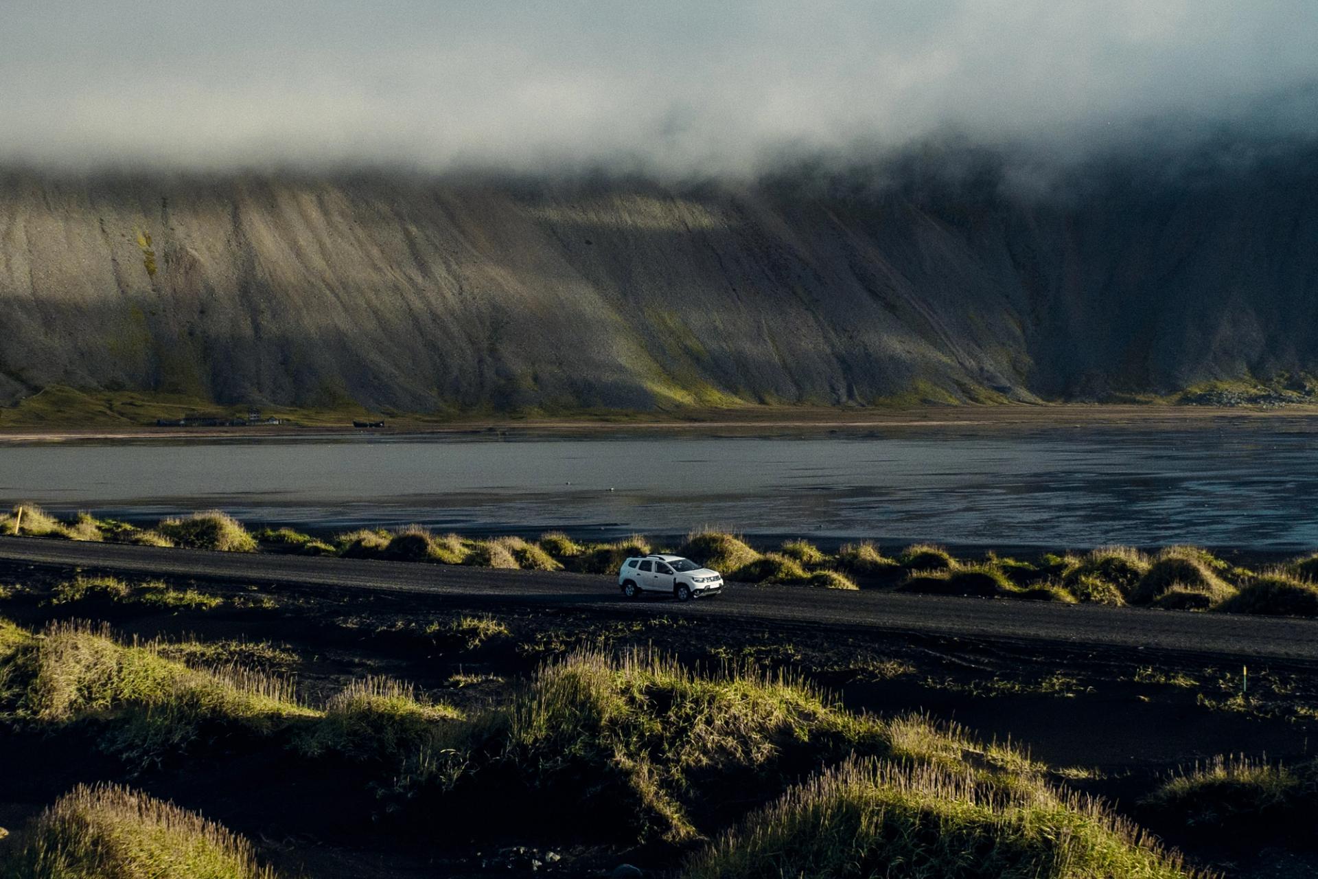 rental car on the road in Iceland in the middle of Icelandic landscapes (mountains, green plains and sea) 