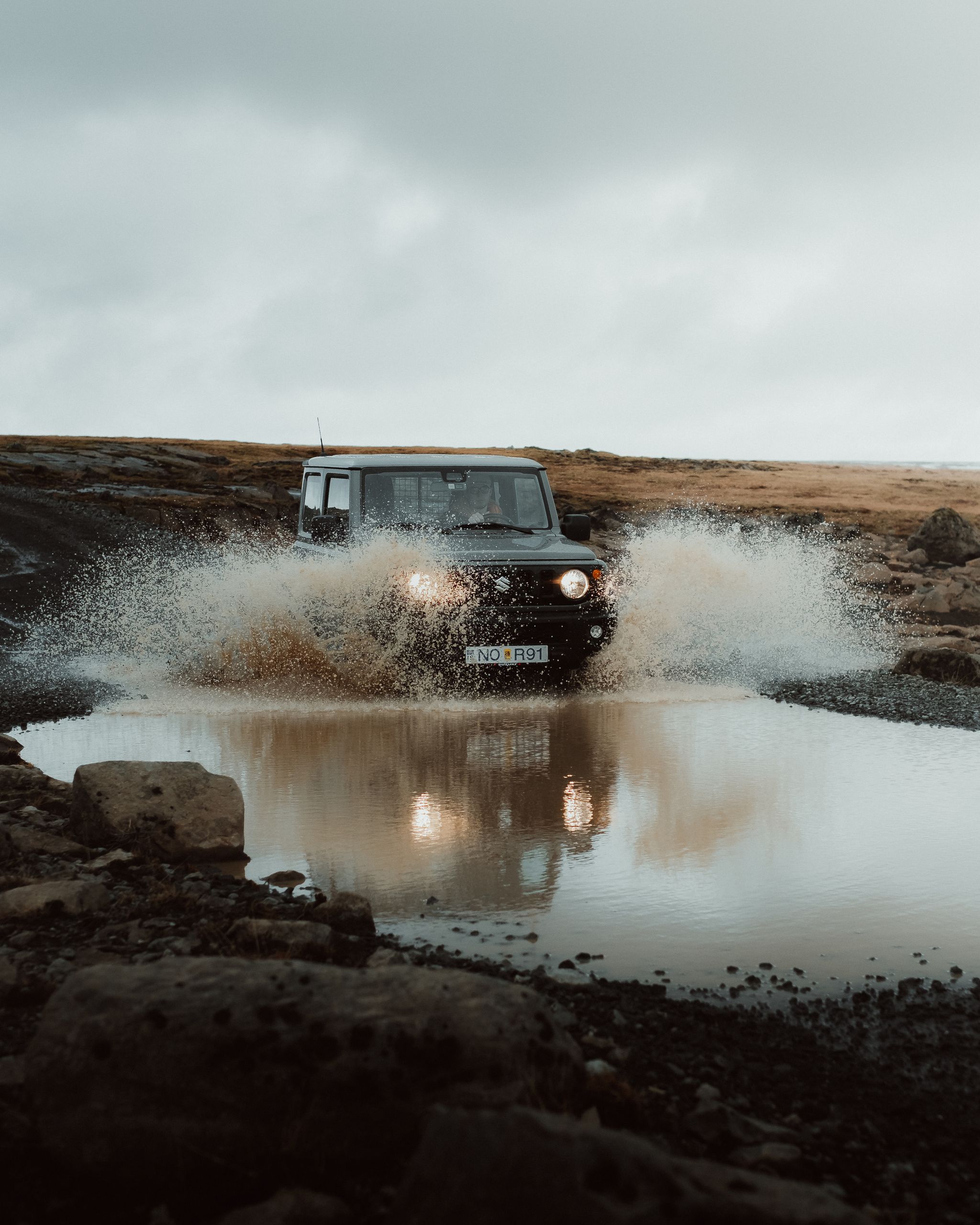 A Suzuki Jimny 4x4 bravely crossing a rushing river in Iceland's rugged terrain