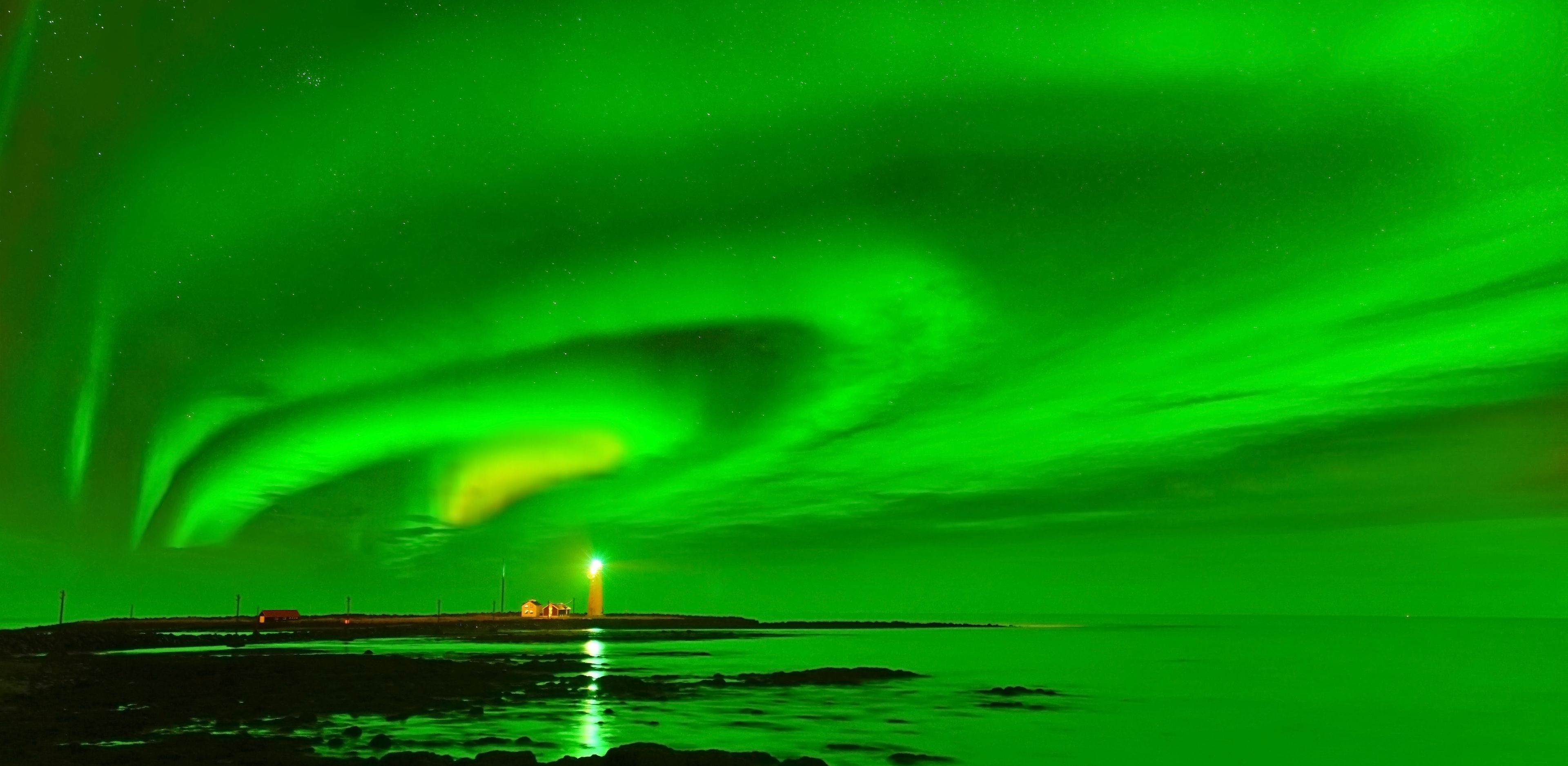view on particularly visible green aurora borealis and the grotta lighthouse lit in the distance 
