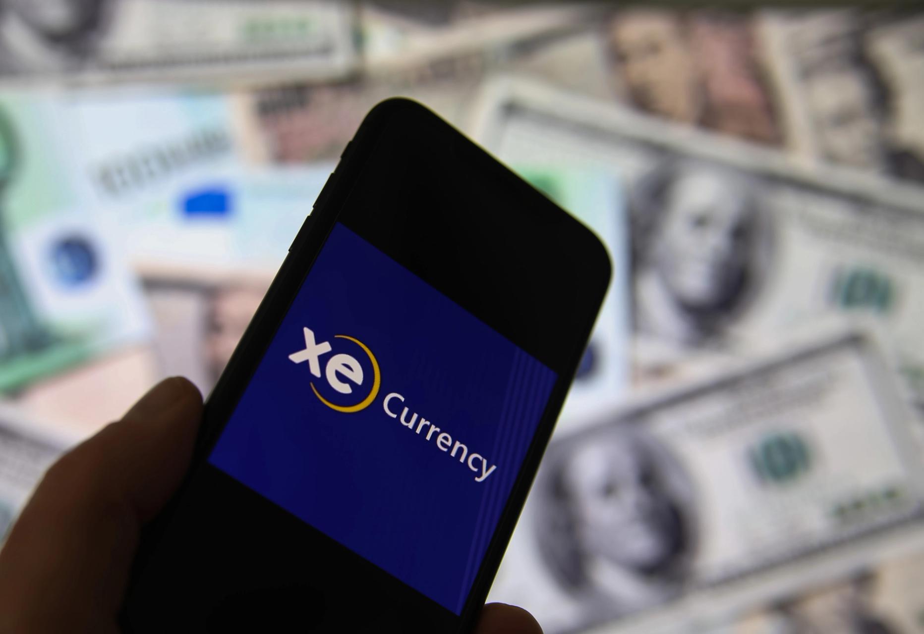 loseup of smartphone screen with logo lettering of online money transfer service xe currency, blurred banknotes