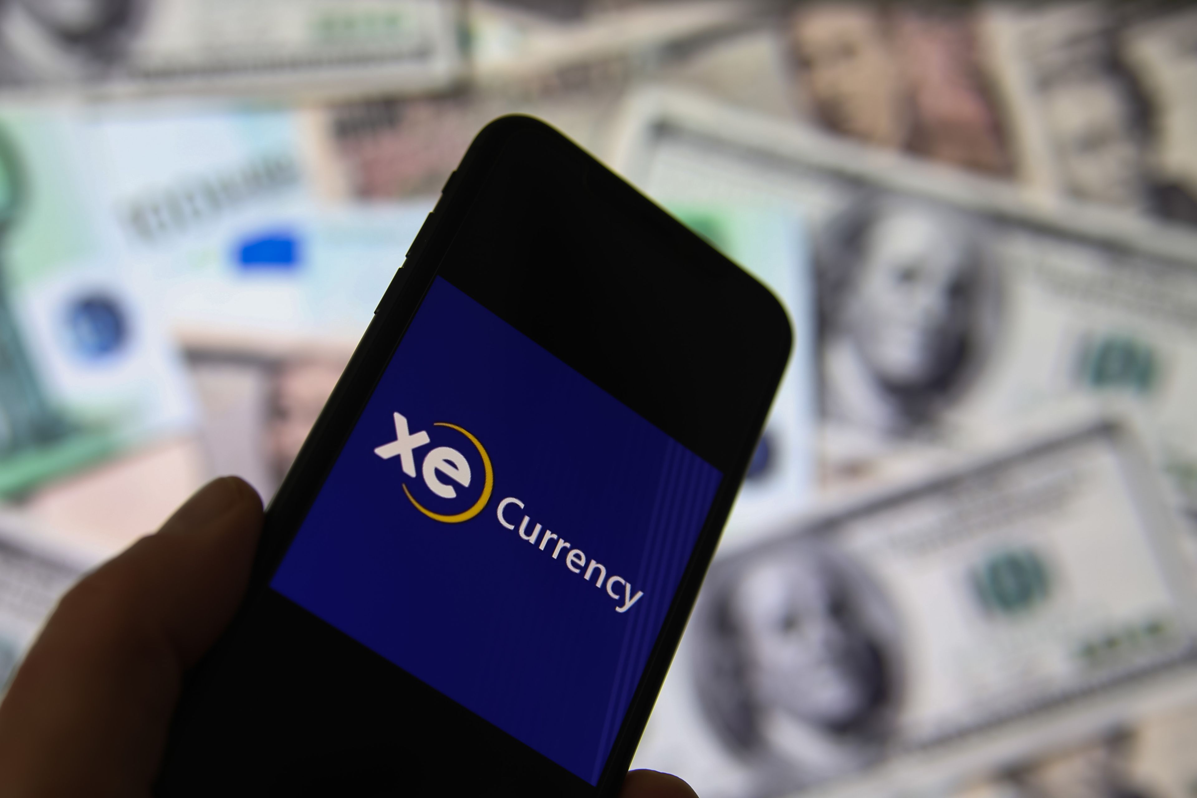 loseup of smartphone screen with logo lettering of online money transfer service xe currency, blurred banknotes