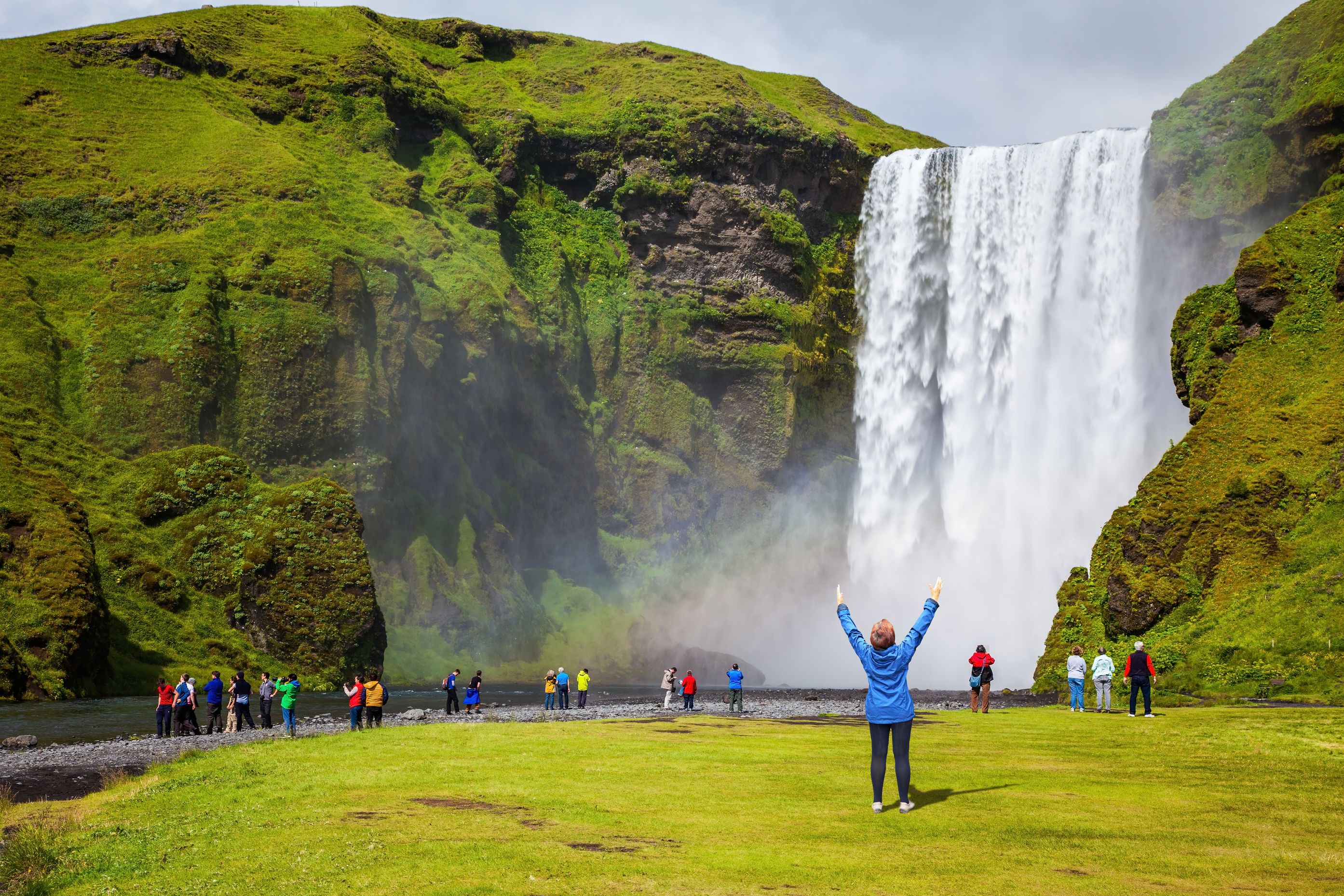 Mujer levantando los brazos en frente de la cascada de Skógafoss, Islandia