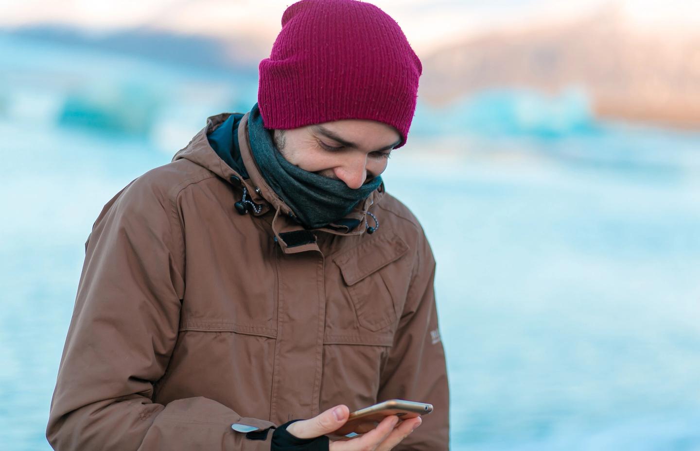 Guy tourist walks in winter in Iceland. looking at his phone with an app open.