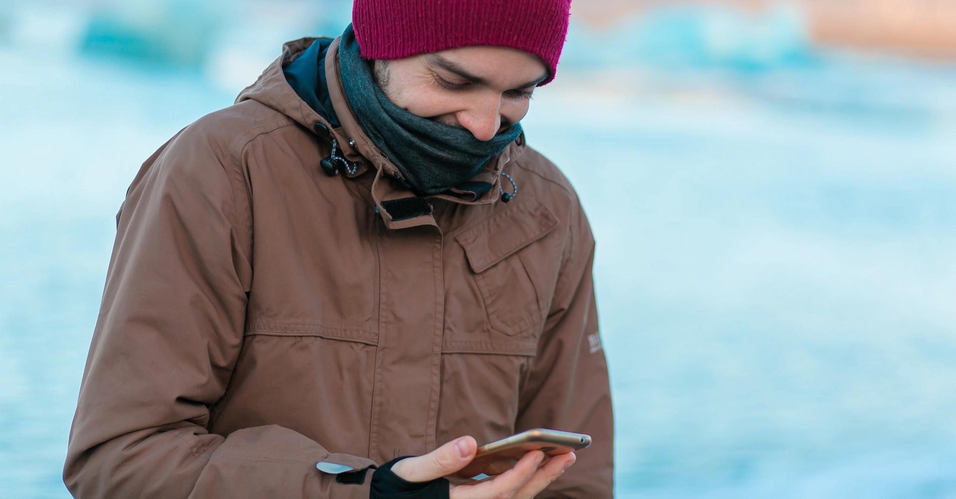 Guy-Touristenspaziergänge im Winter in Island. schaut auf sein Telefon mit geöffneter App.