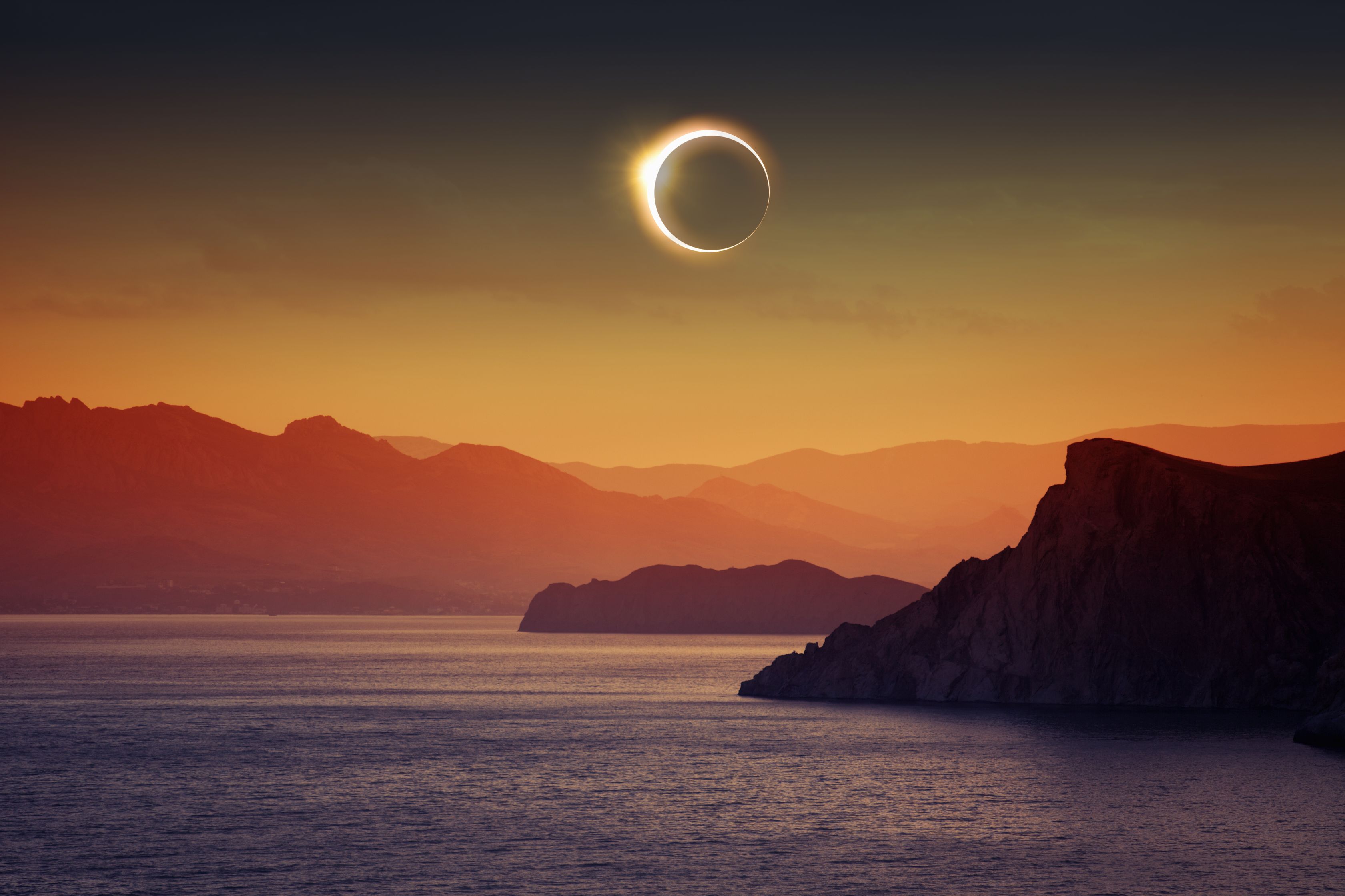 Solar eclipse above lake and mountains