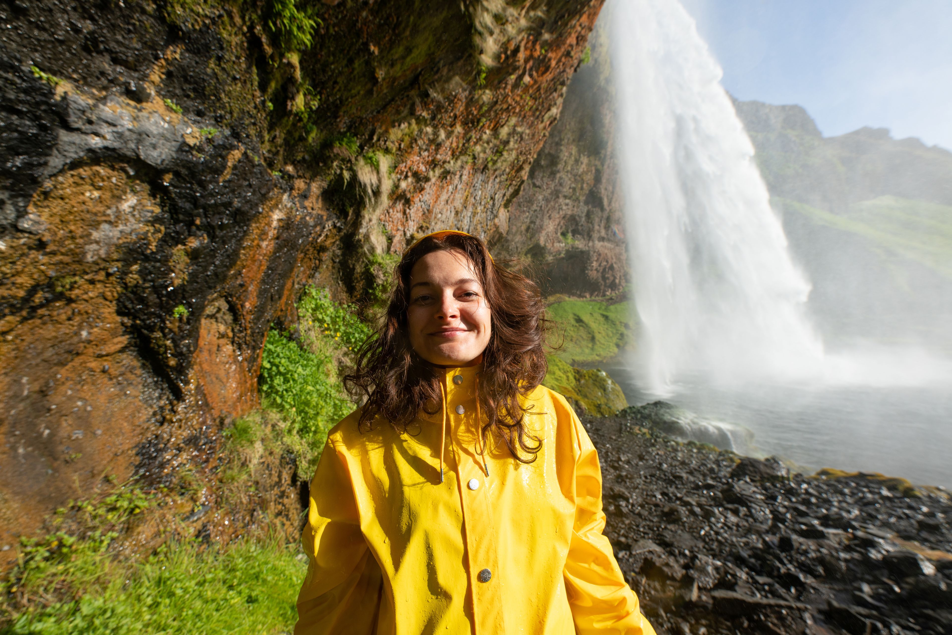 woman wearing a yellow rain jacket near seljalandsfoss waterfall in iceland