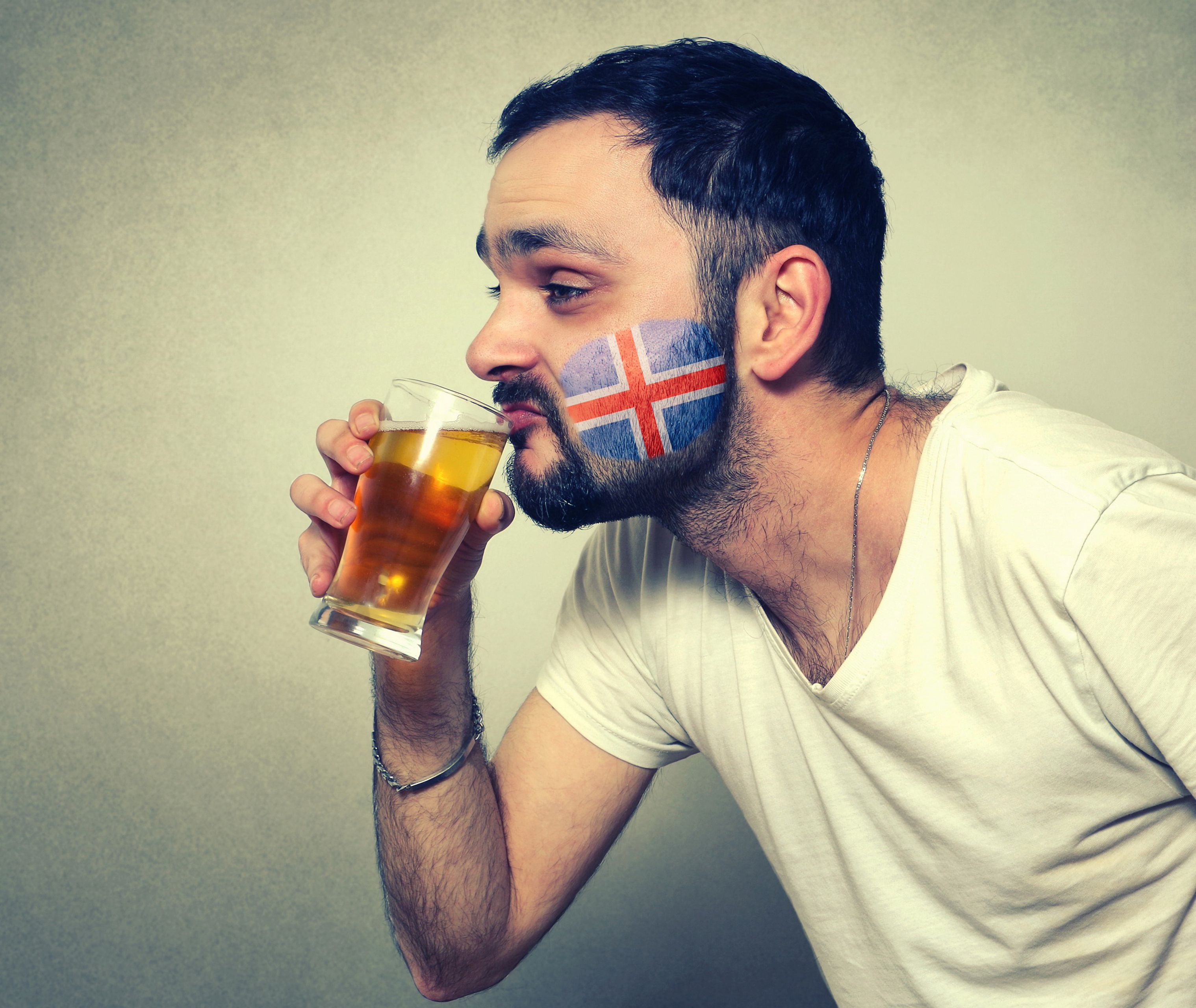 Man with an Icelandic flag painted in the face drinking a beer