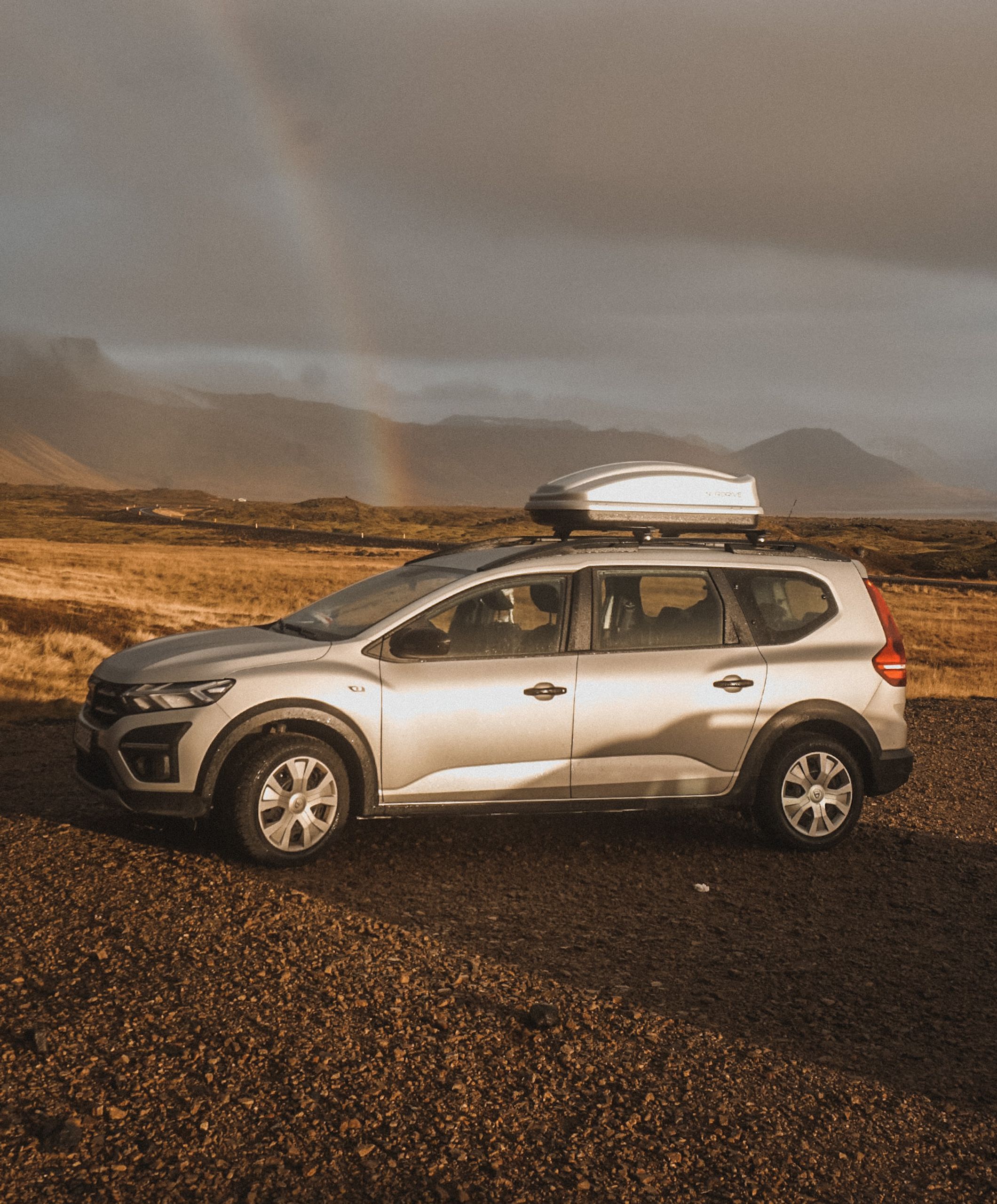 Dacia Jogger with a rood box parked with a rainbow in the background