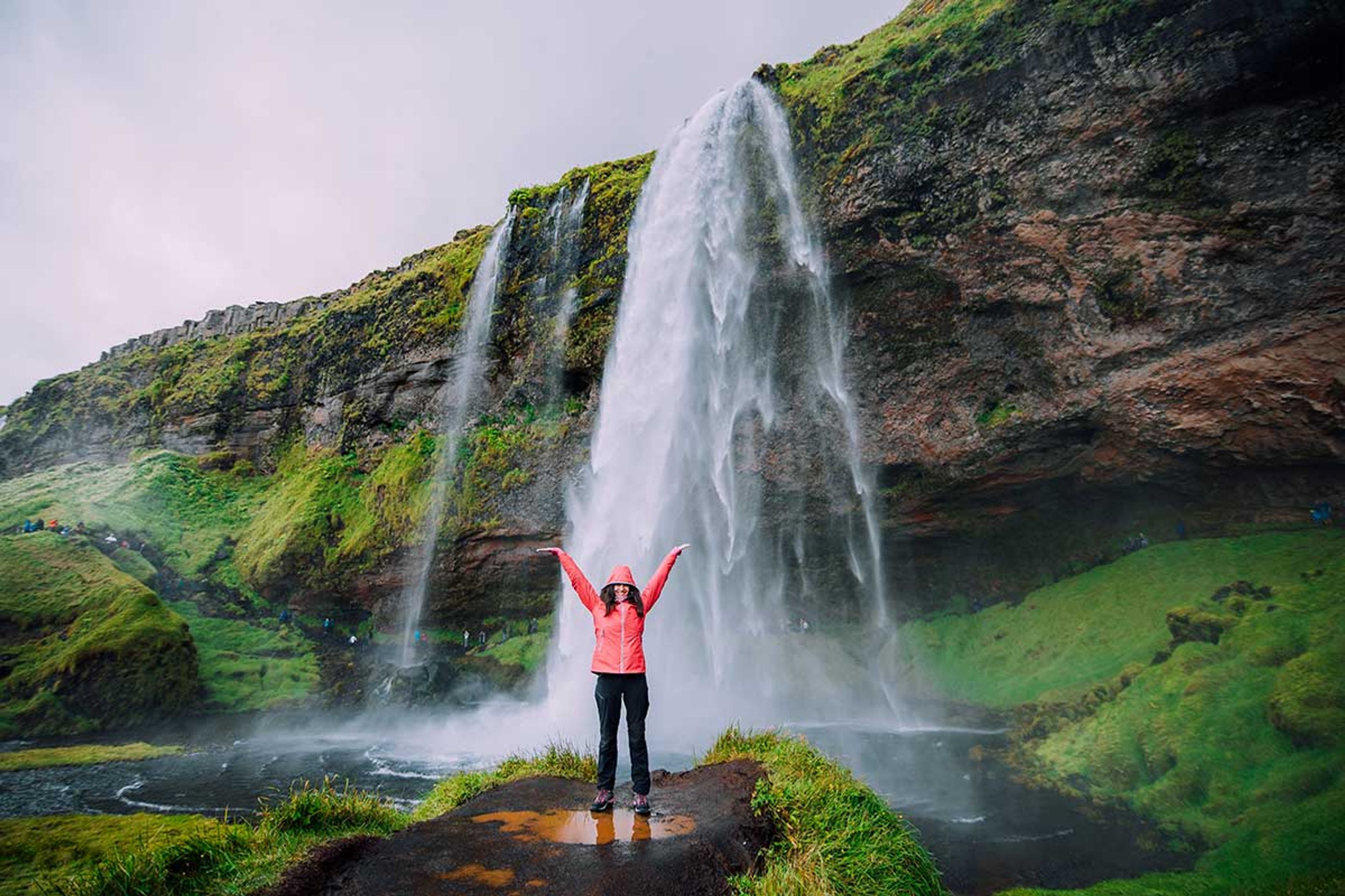 Woman in front of one of the waterfalls of Iceland, happy to discover the country and its sumptuous landscapes 