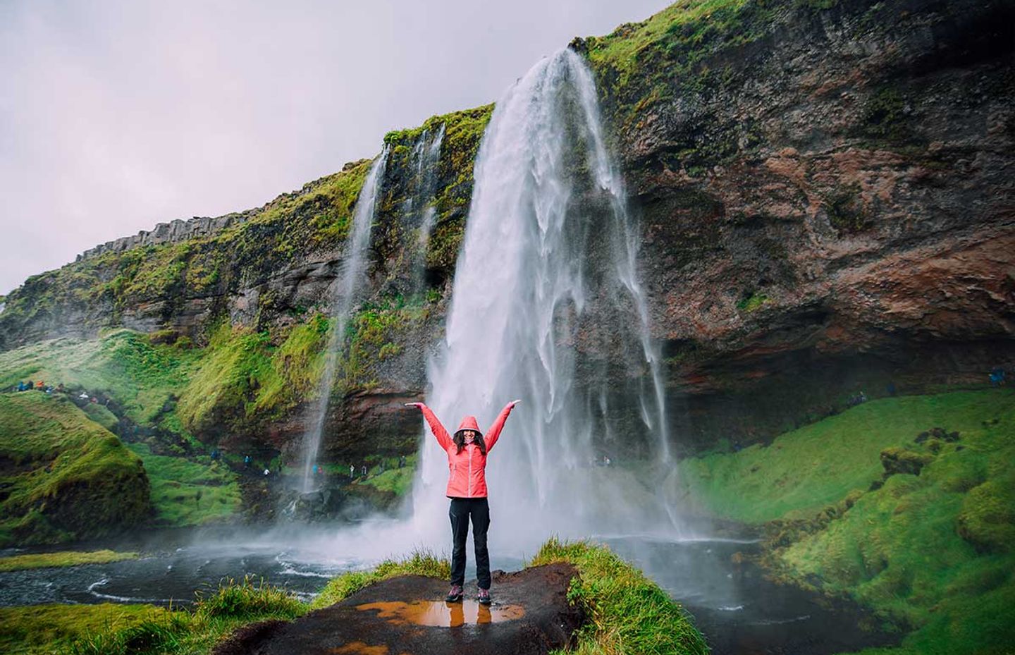 Woman in front of one of the waterfalls of Iceland, happy to discover the country and its sumptuous landscapes 