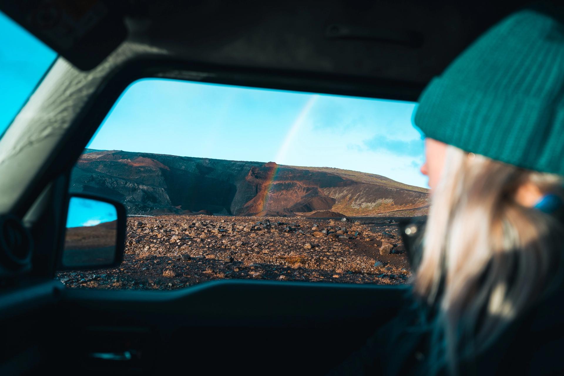 A woman relaxing in her rental car while watching a rainbow