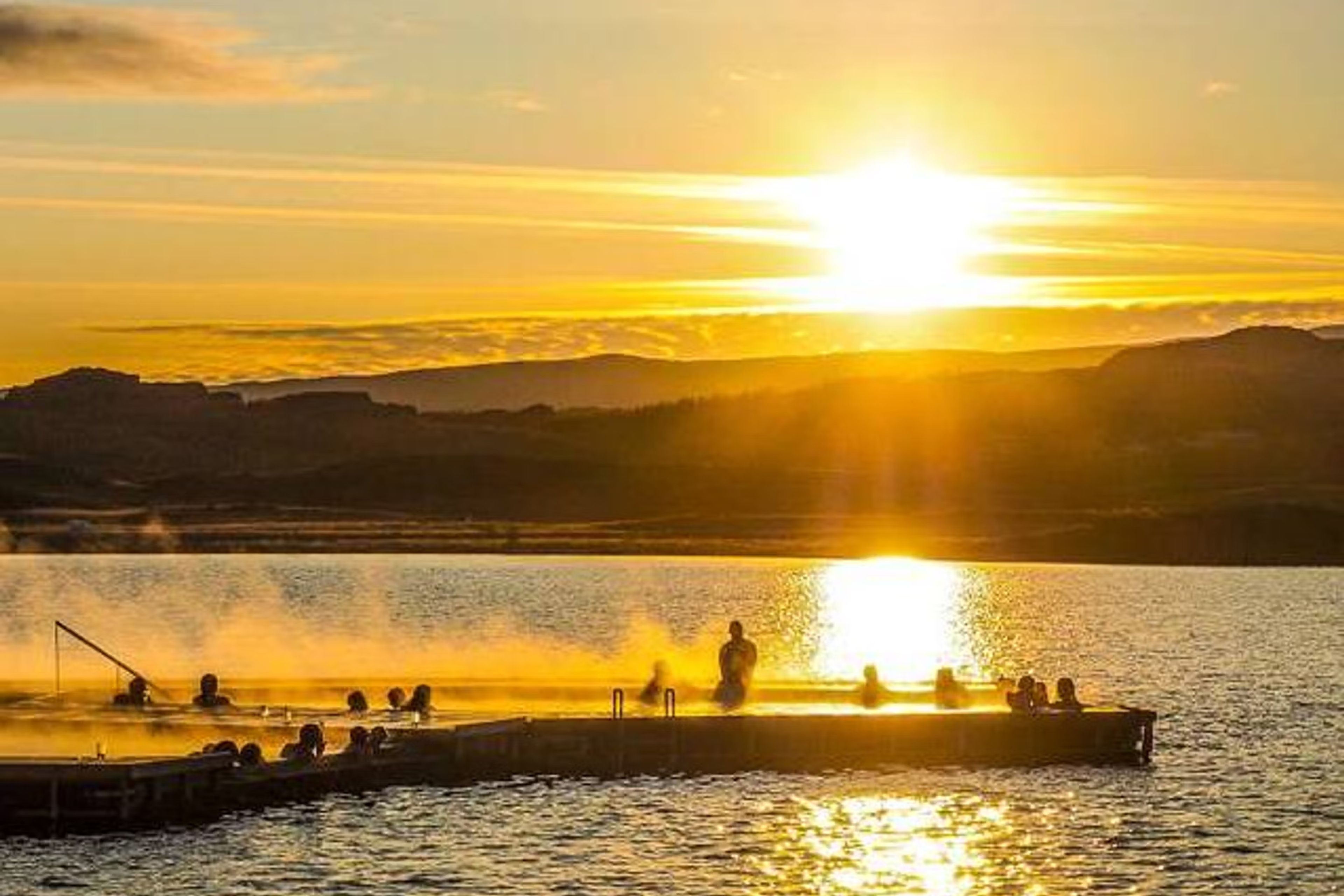 Vök Baths with people inside and the sun about to set