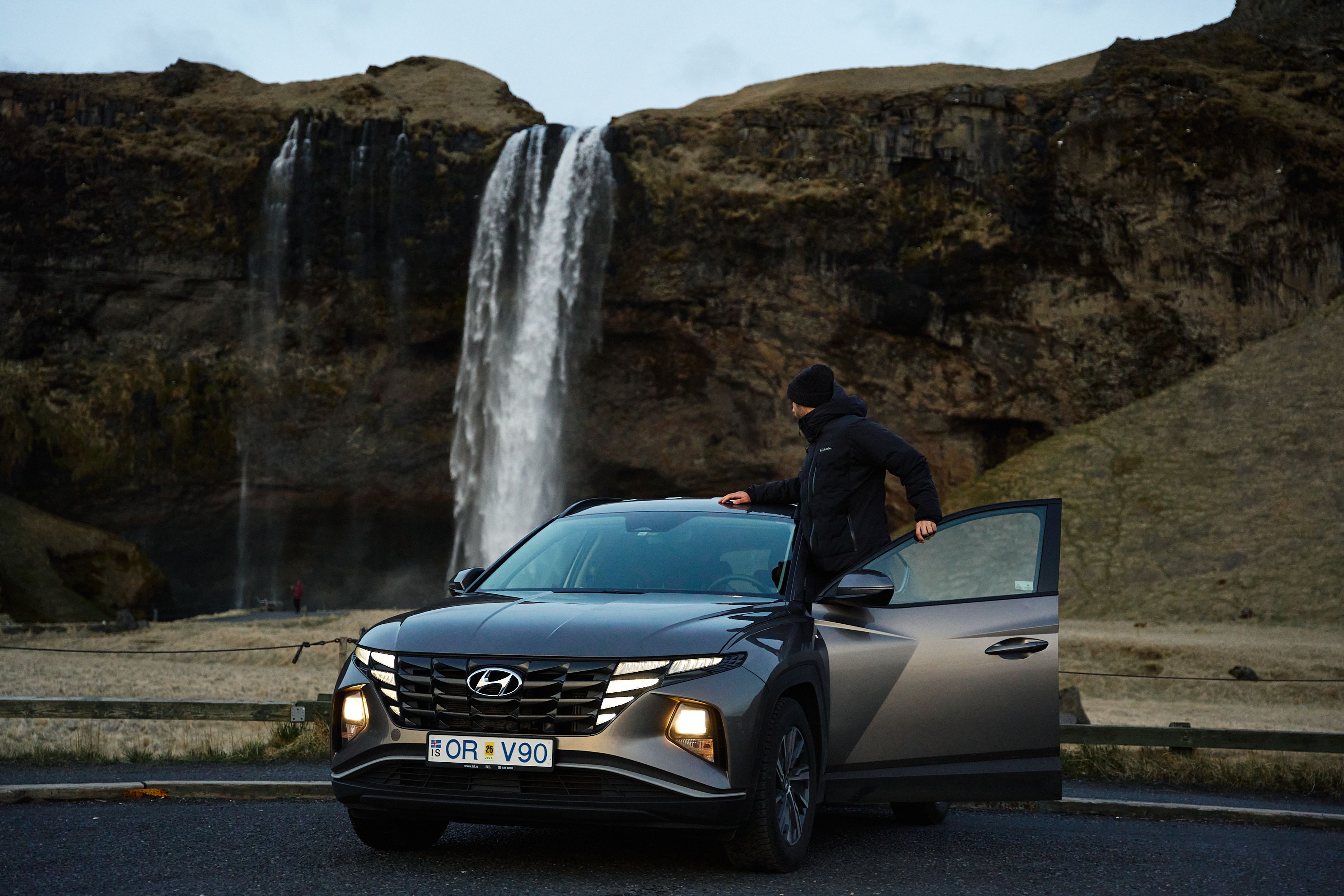 A man standing next to his rental car while looking at a waterfall