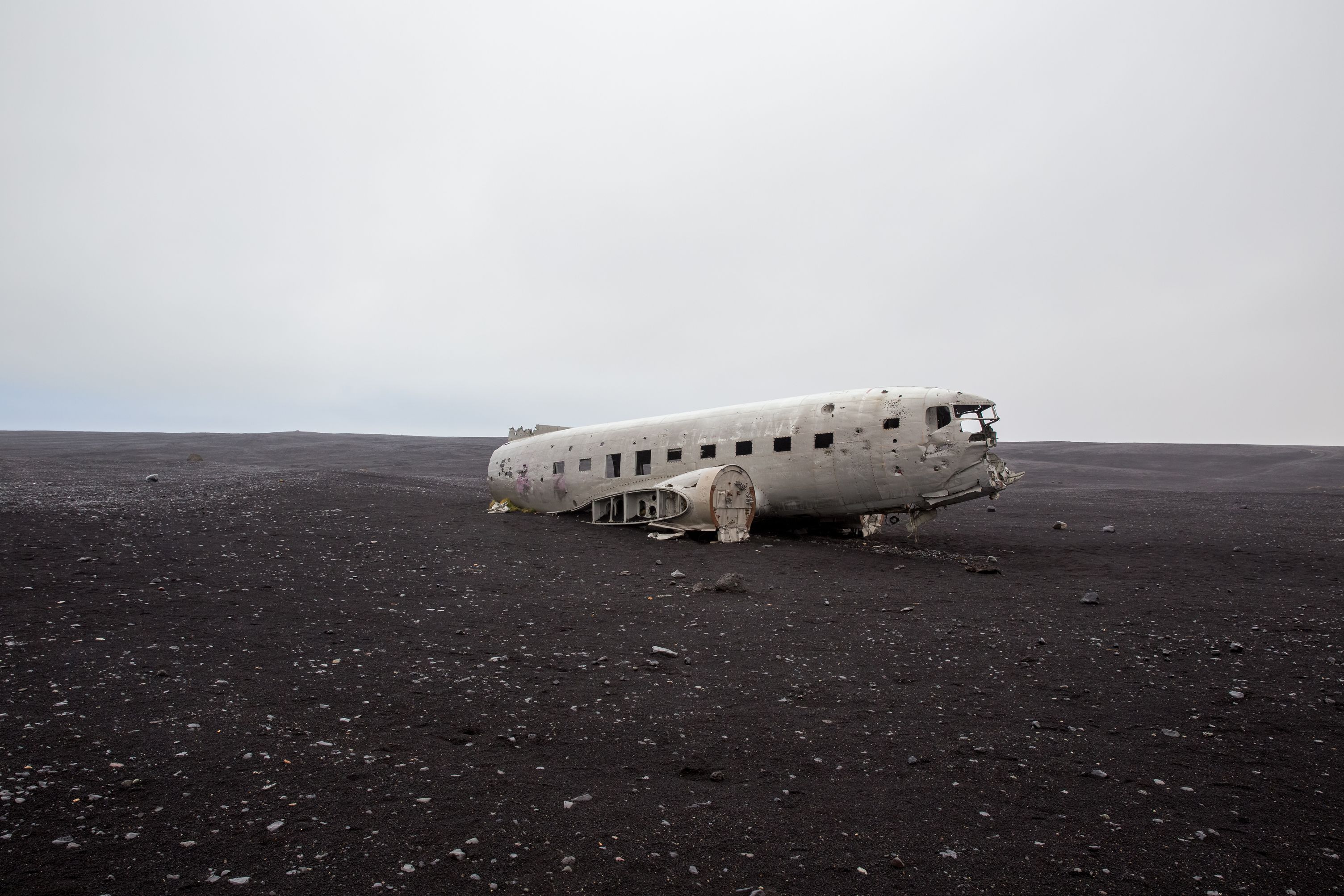 An aerial view of the abandoned DC plane on Solheimasandur beach in Iceland. The plane rests in the middle of a vast black sand beach.