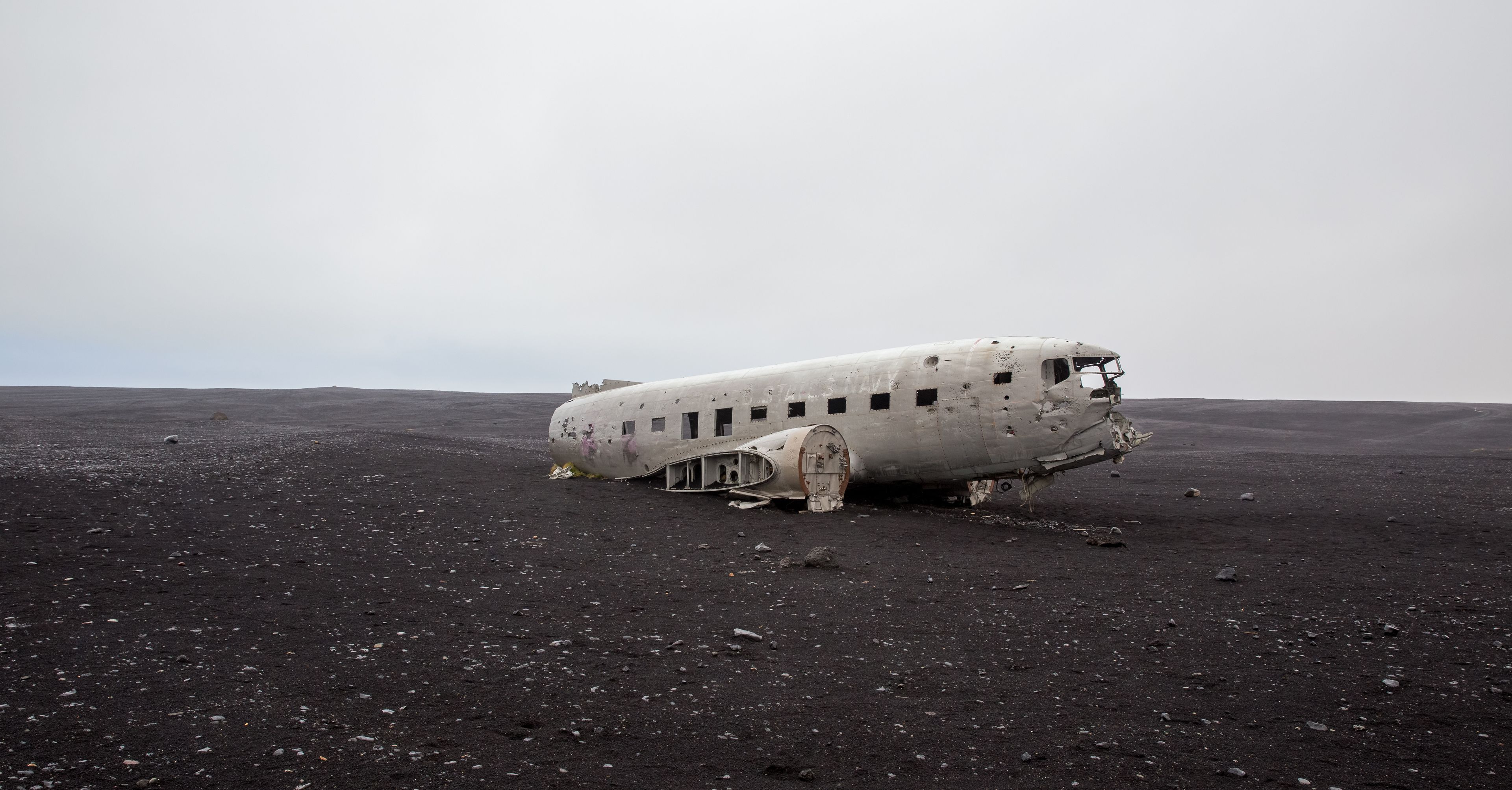 An aerial view of the abandoned DC plane on Solheimasandur beach in Iceland. The plane rests in the middle of a vast black sand beach.