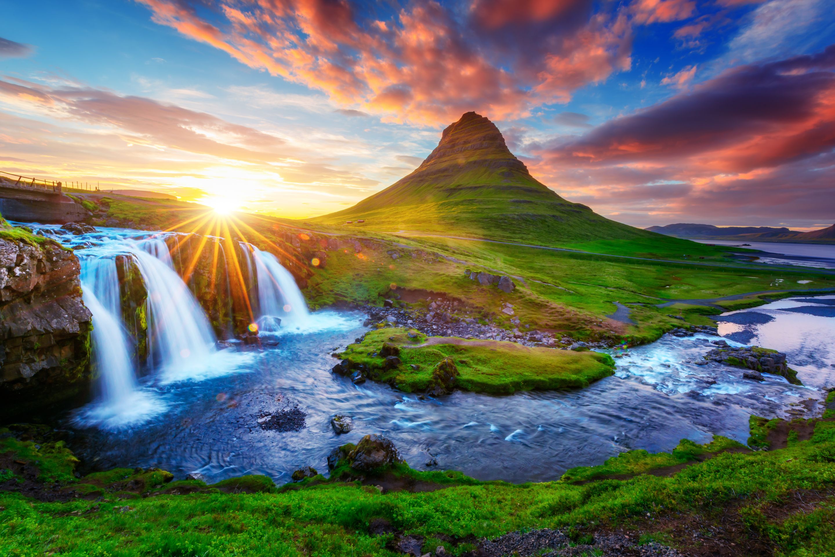 冰岛的绿山，背景是夕阳，前景是瀑布。