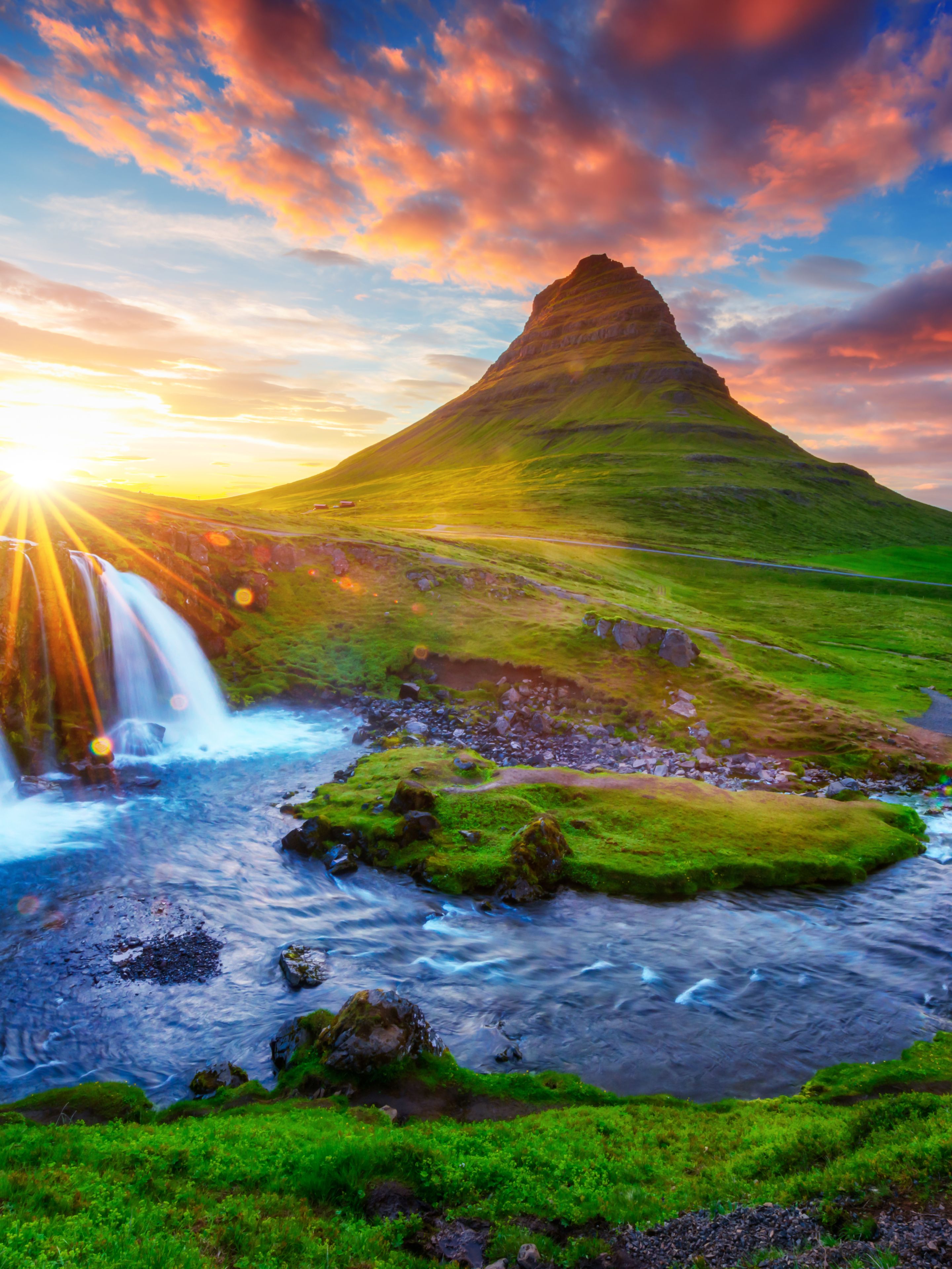 Montagne verte en Islande avec un coucher de soleil en arrière-plan et une cascade à l’avant