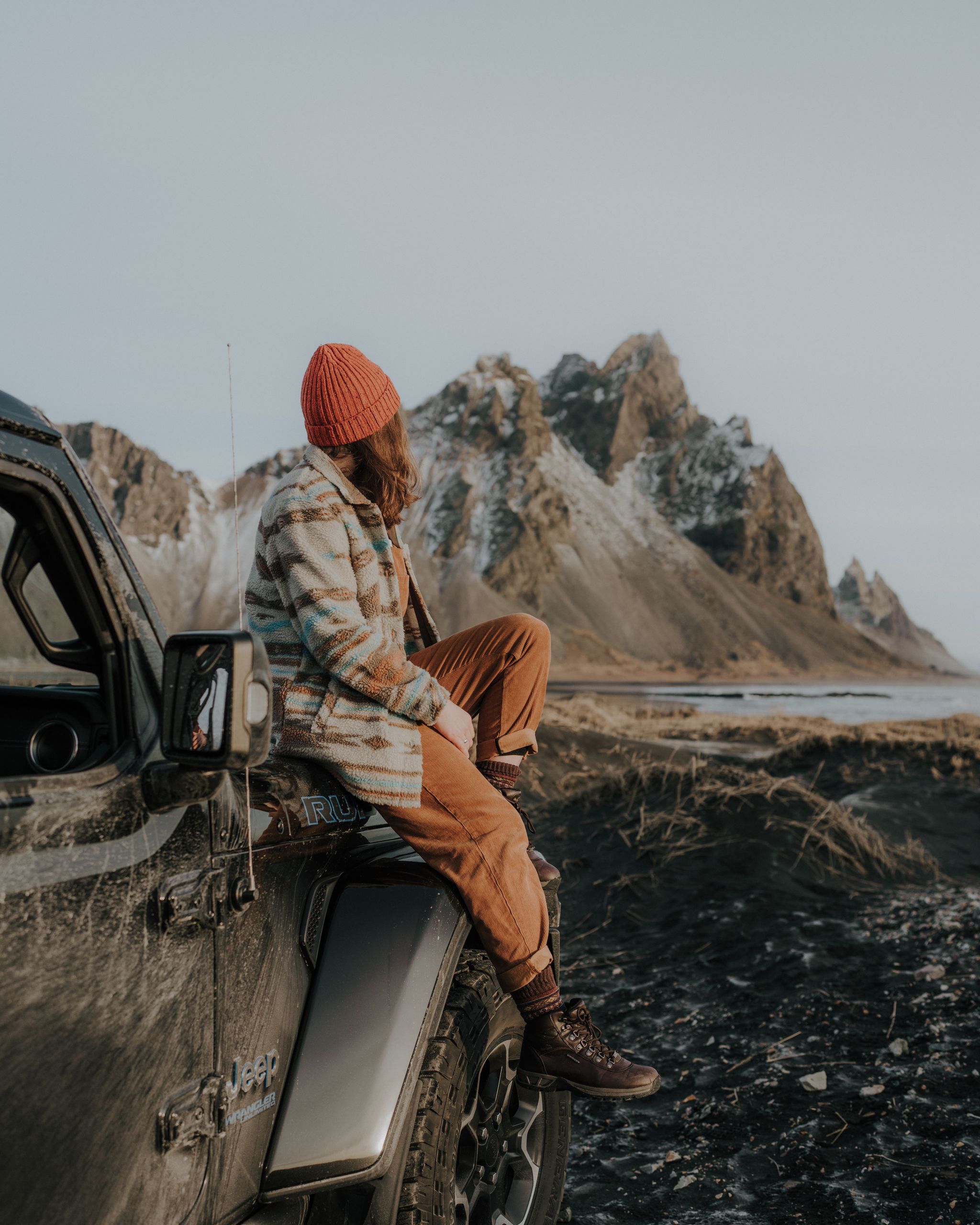 Girl sitting in the front of her car with mountains in the background