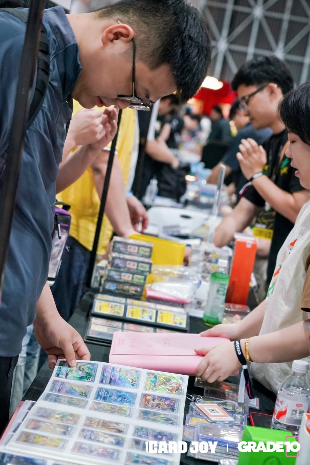 Collectors browsing binders of trading cards at a dealer table.