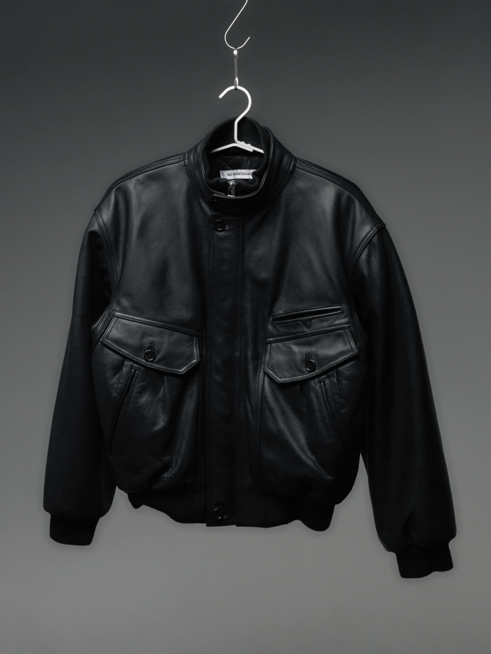 A black leather bomber jacket with large front pockets, hanging on a hanger.