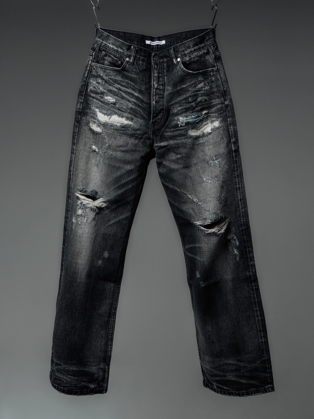 Distressed dark grey jeans with large rips and fading, hanging.