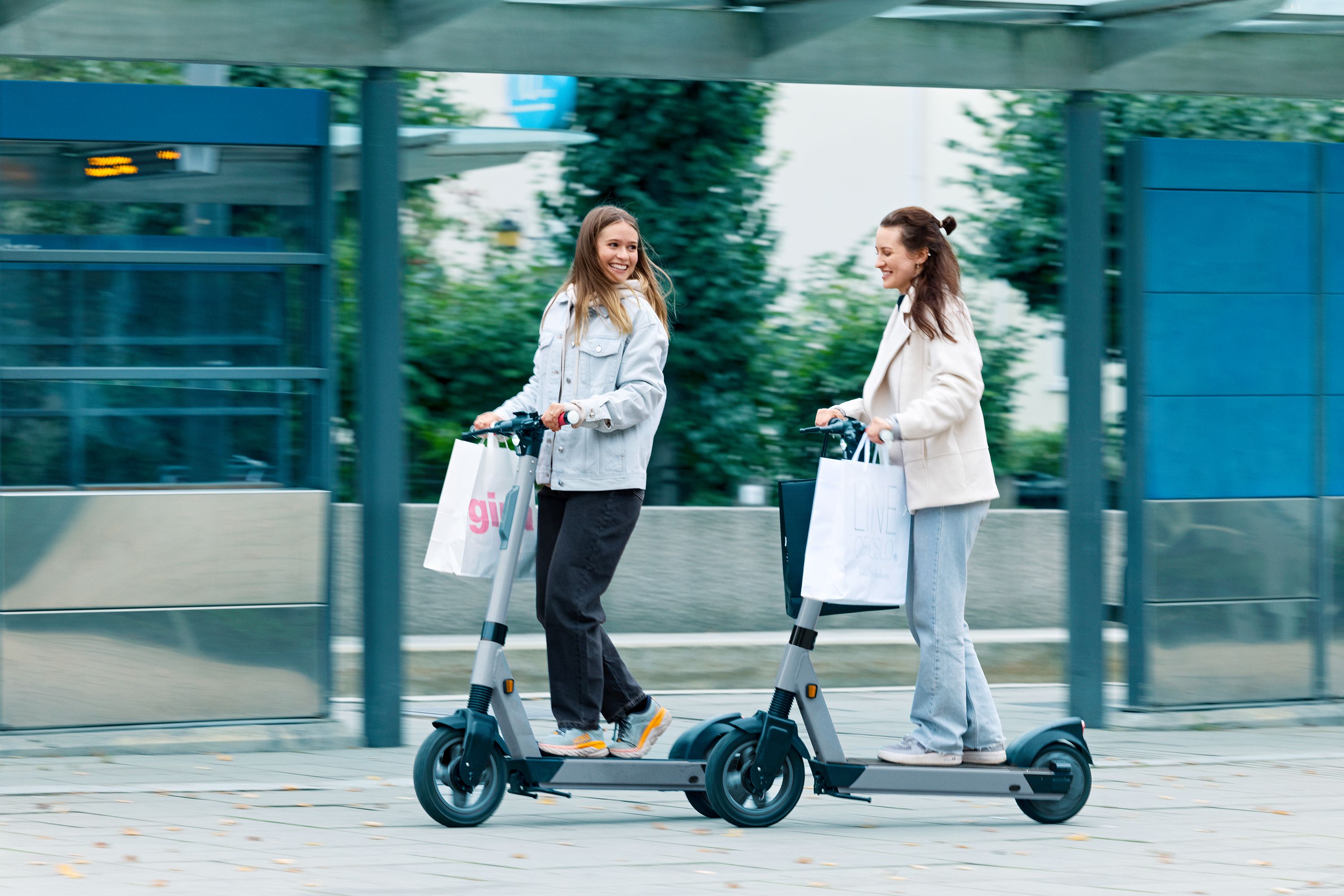 To personer kjører elsparkesykler ved trikk holdeplass