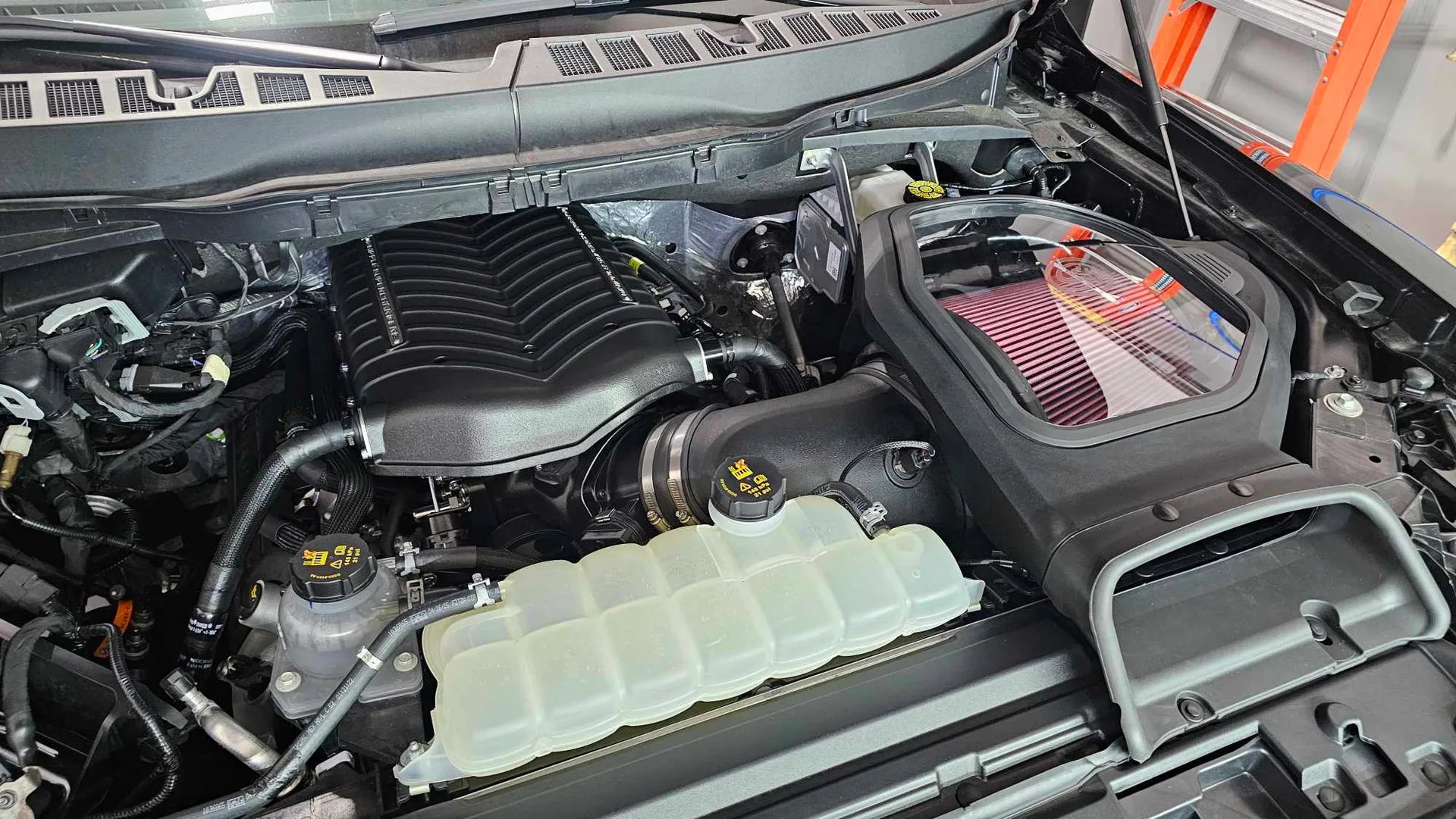 A view of the engine bay of a Ford Raptor R with a supercharger upgrade and cold air intake.