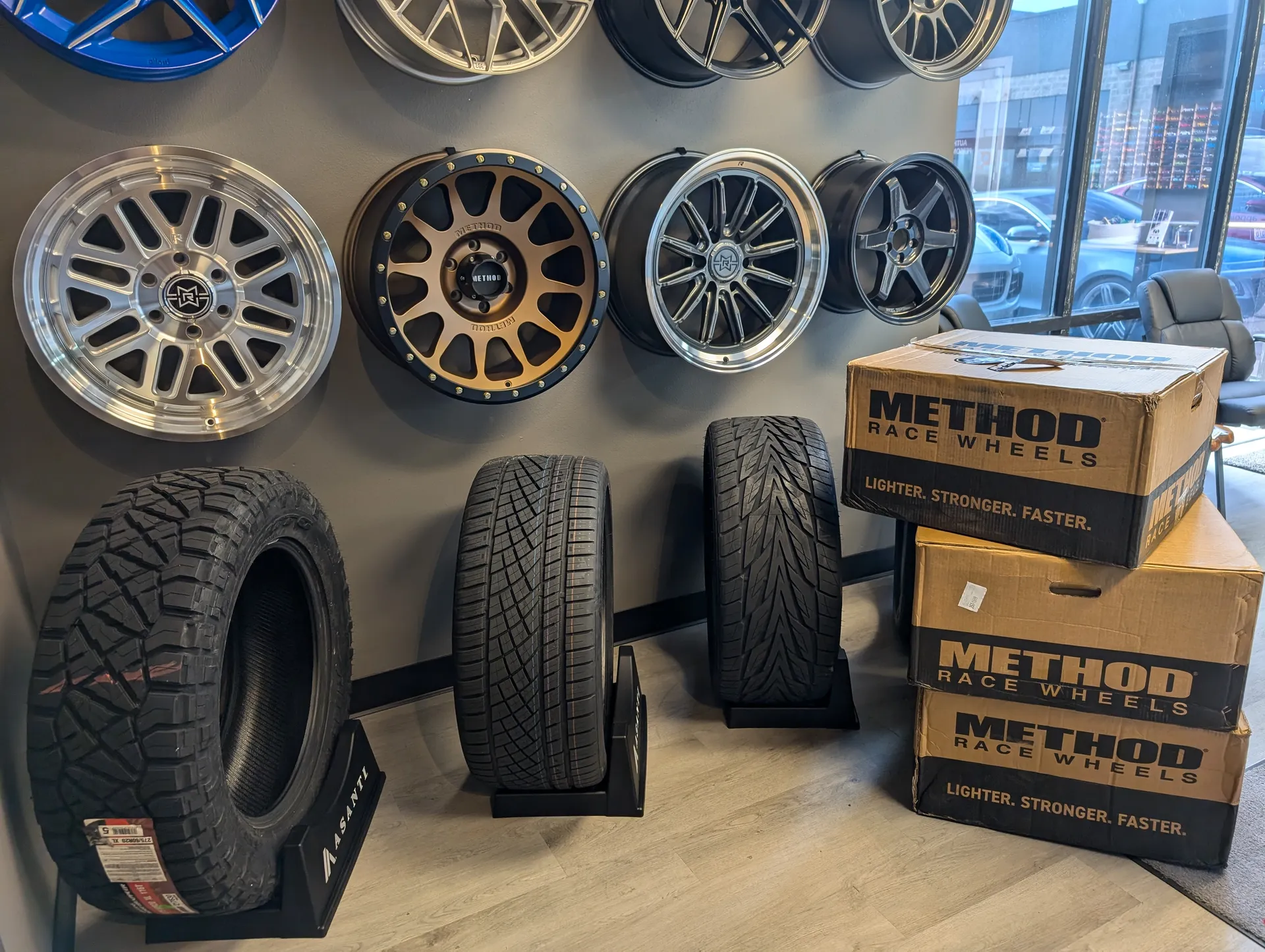 Inside the front office area. The wall is decorated with custom wheels. There are different tire styles displayed. A fresh set of wheels still in boxes are next to the tire display.