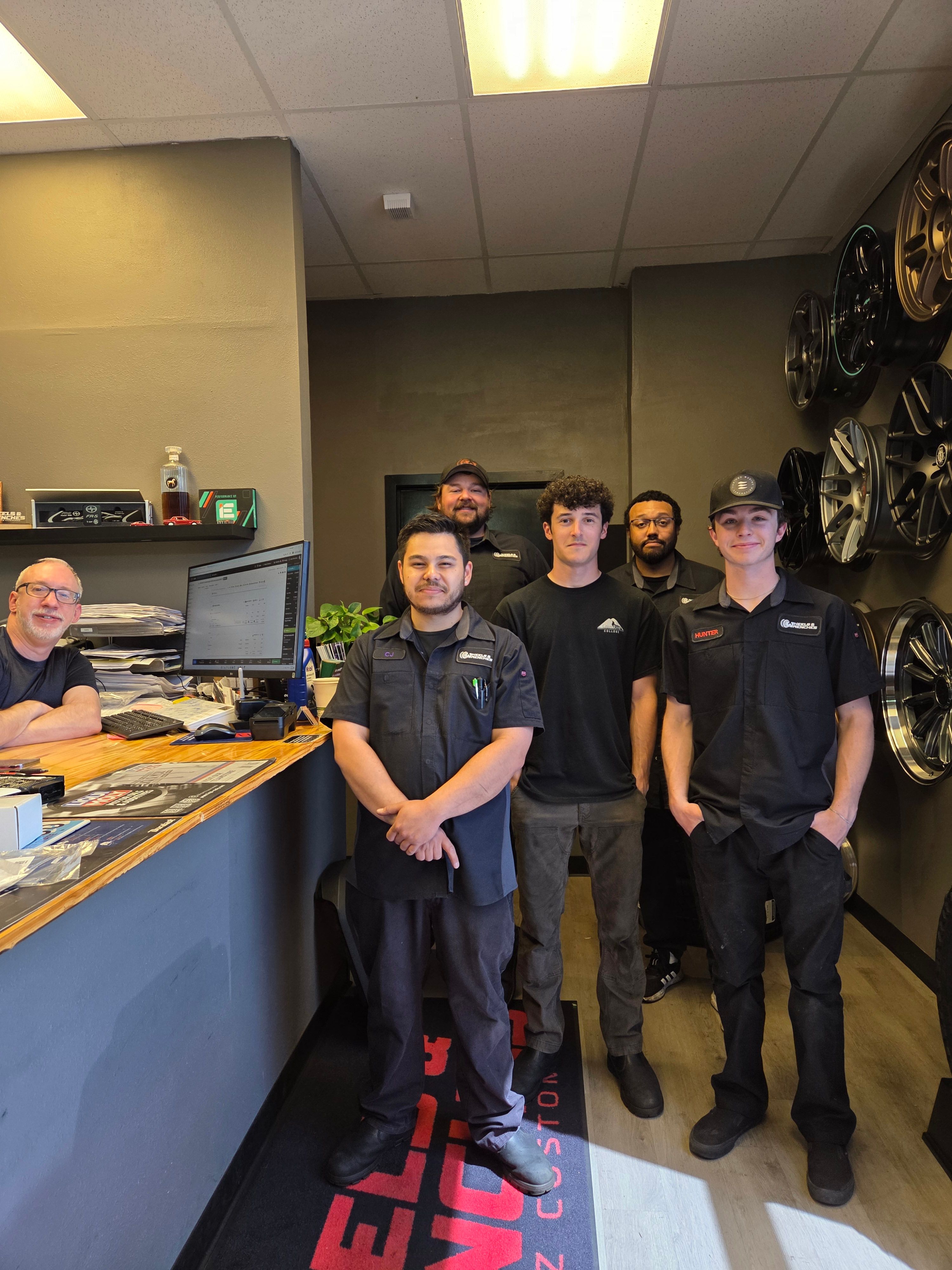 The team at Wheel & Wrenches smiling for a group photo in the shop's front office area.