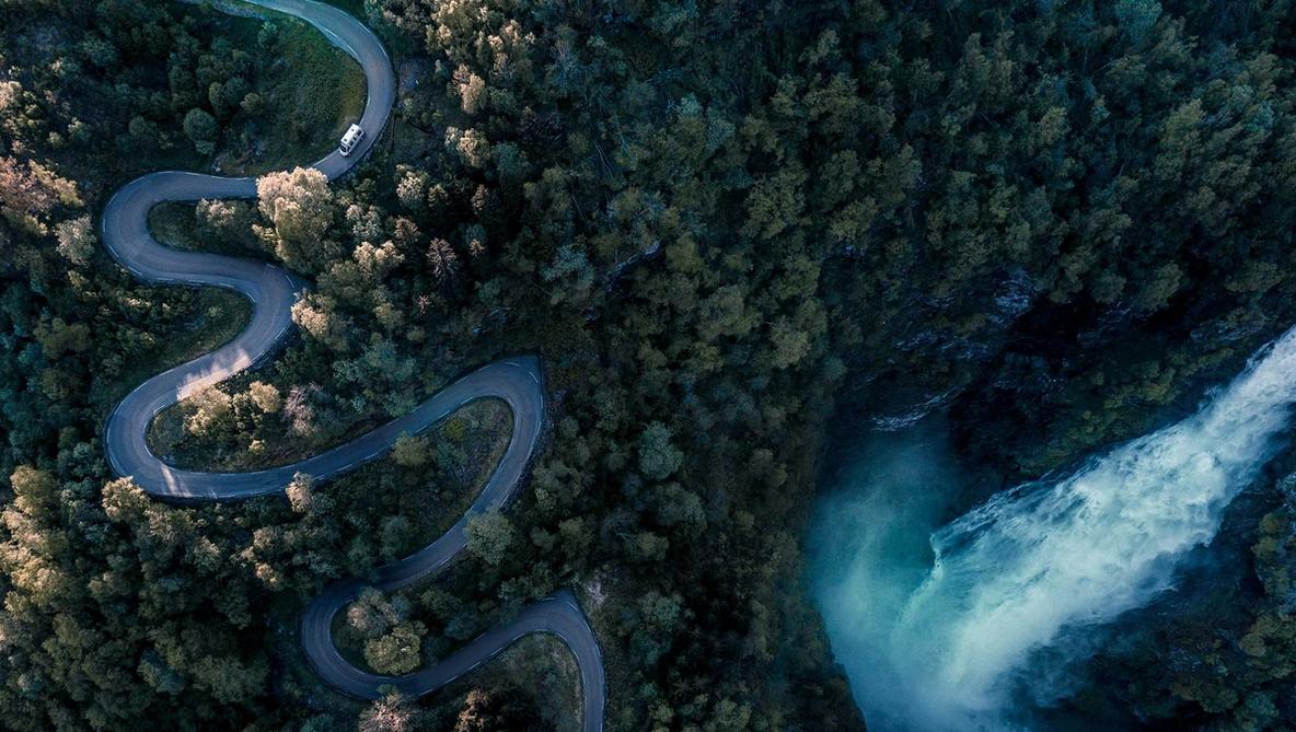Overhead shot of a vehicle driving down a hairpin road with a waterfall