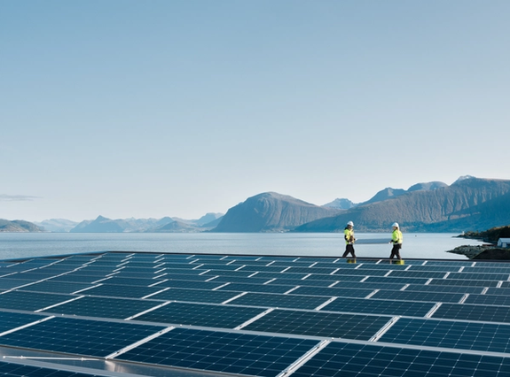 Two people walkin on a solar panel roof  with mountains and ocean in the background