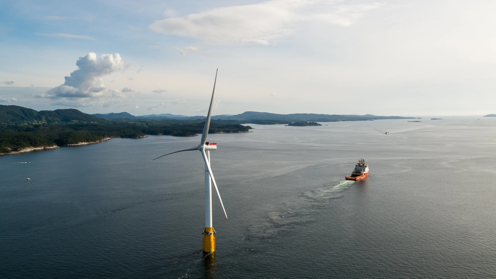 Offshore wind turbine at sea along coastline, with service vessel
