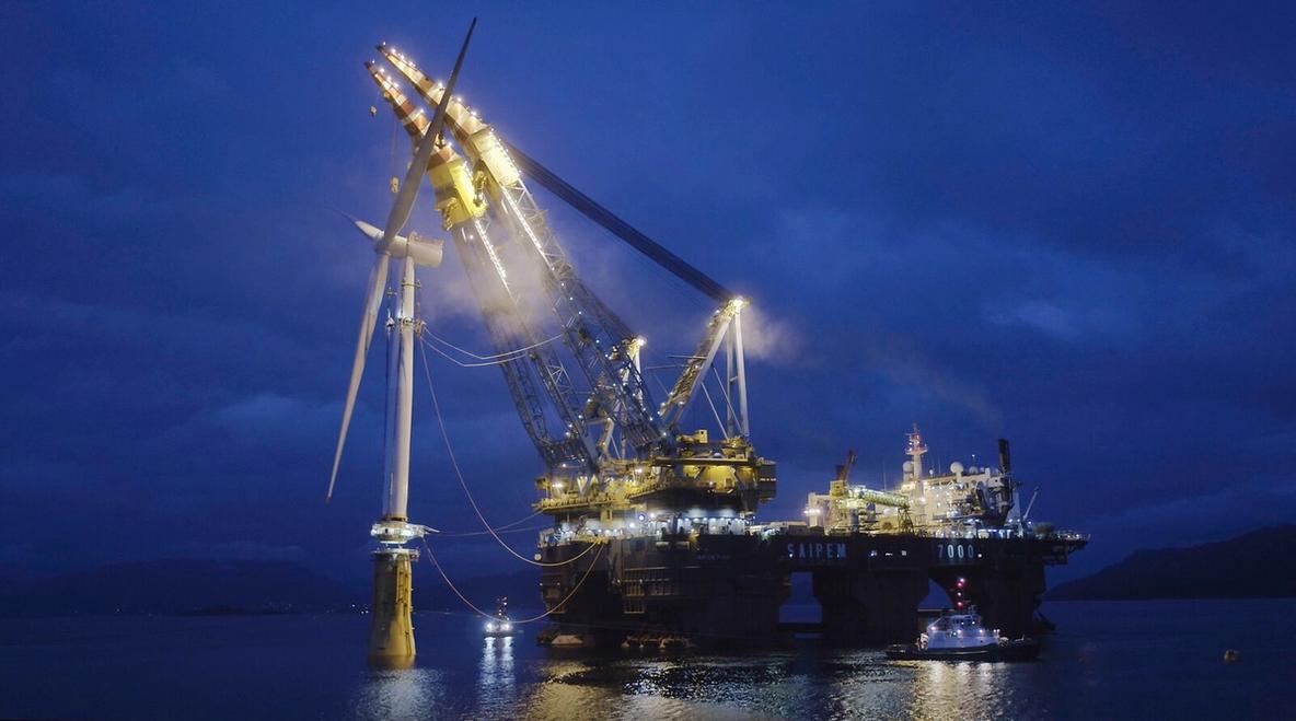 Large installation platform with crane installing Equinor floating offshore wind turbine at night