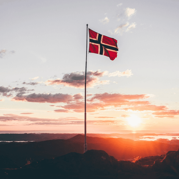 Norwegian flag on top of a mountain in the sun set