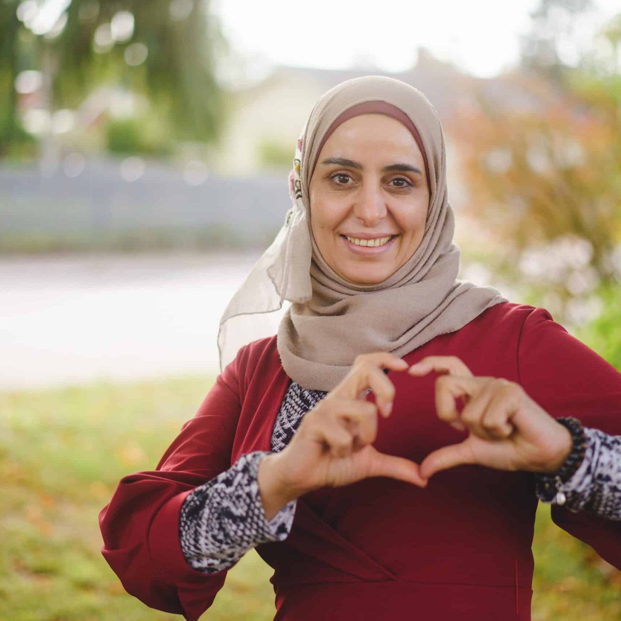 En kvinna i slöjda gör ett hjärta med händerna och ler mot kameran