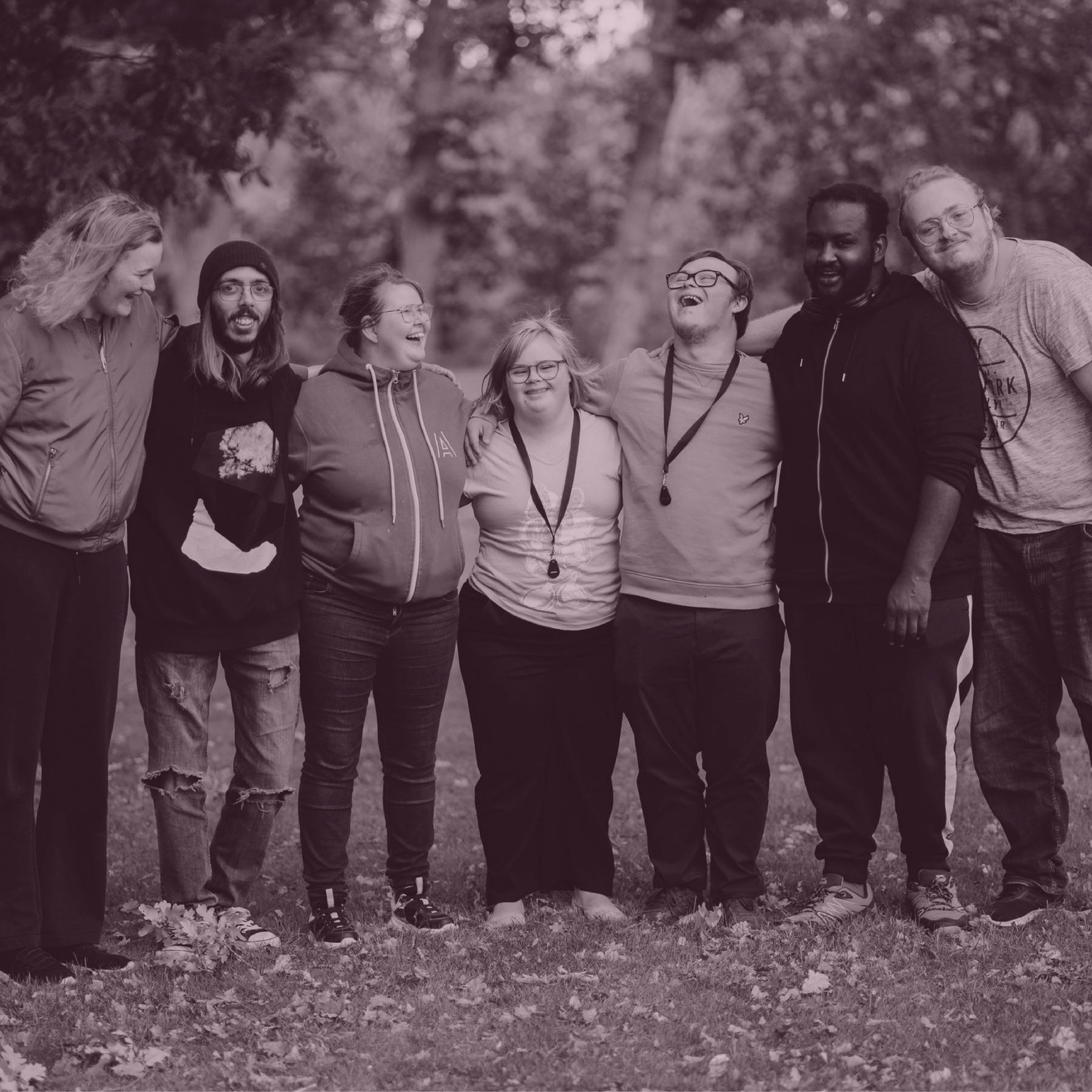 Sju personer står under stora ekar och skrattar tillsammans.