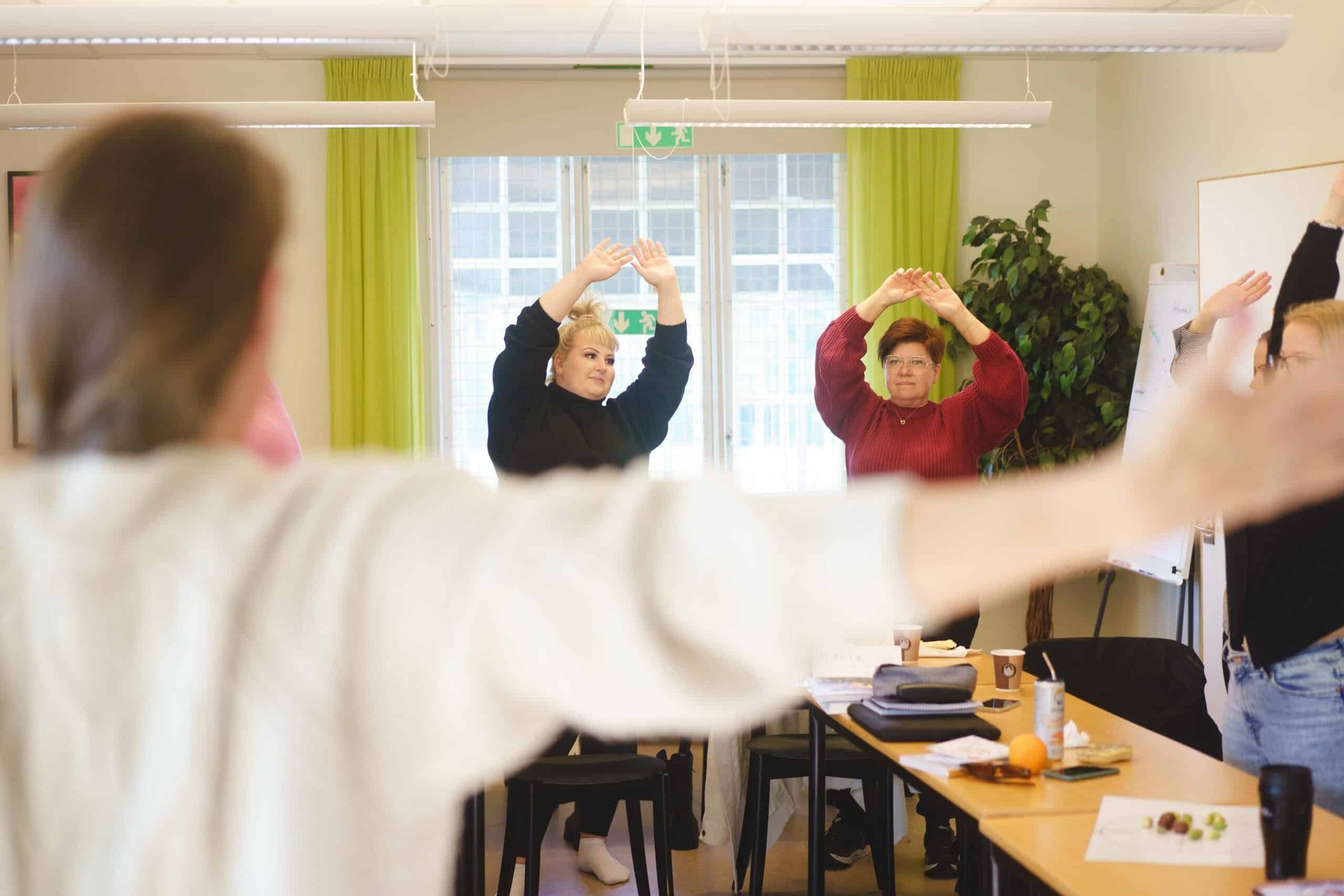 En grupp deltagare gör paus-gympa i ett klassrum. 